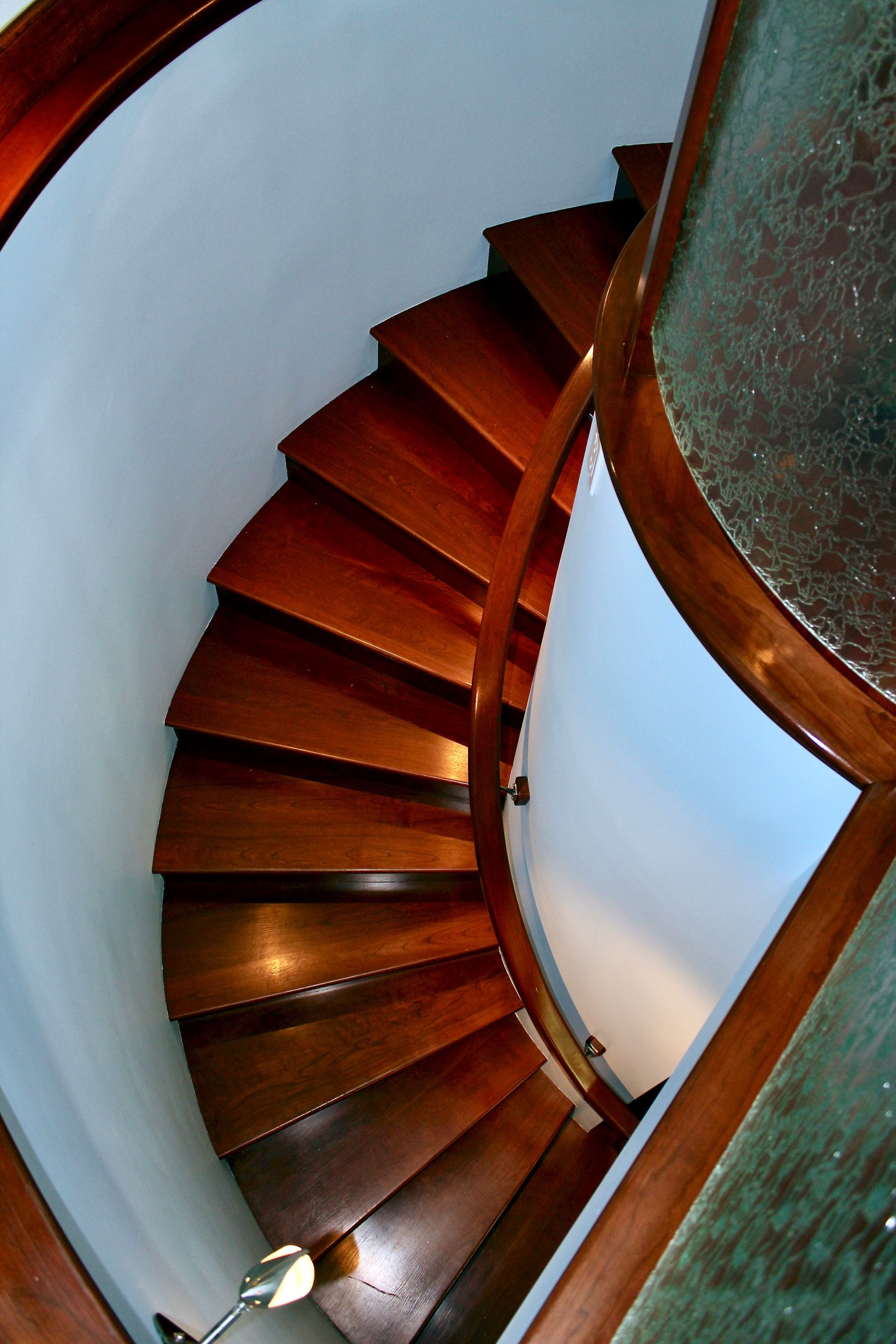 Curved wooden spiral staircase with dark cherry wood steps and a white wall 