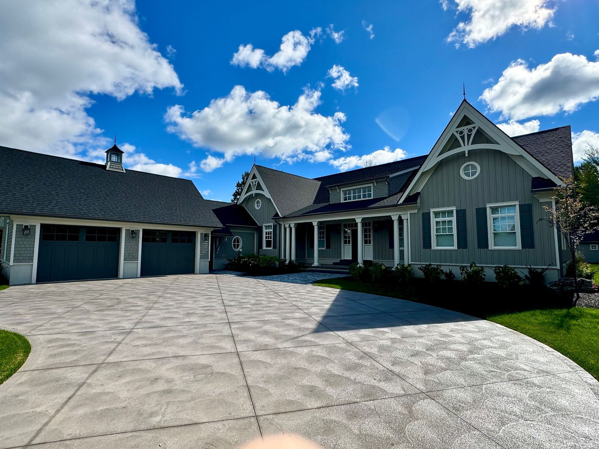 Large gray house with a two-car garage and curved concrete driveway under a bright blue sky.