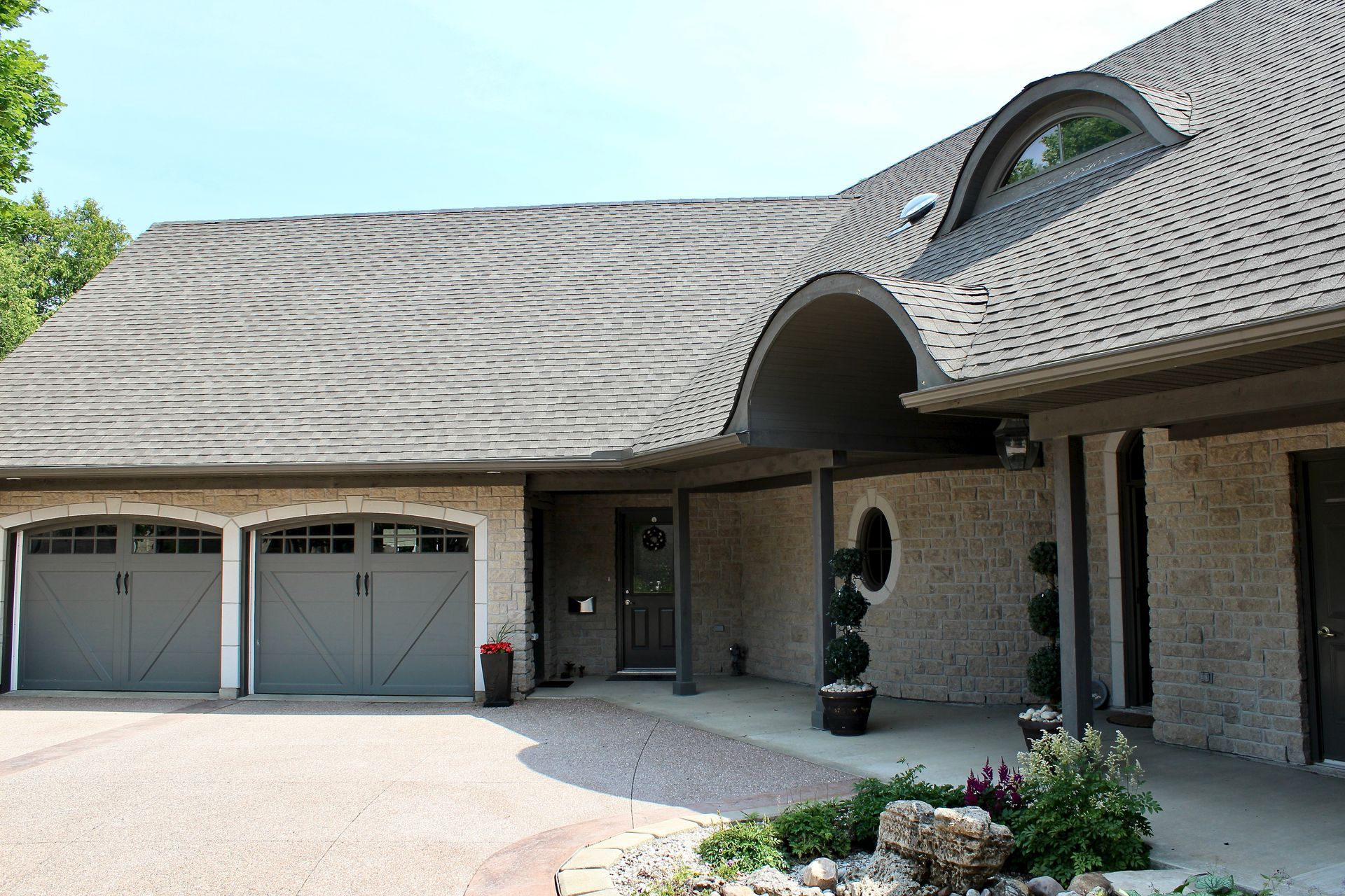 Suburban brick house with double garage, curved dormer window, and arched entryway.