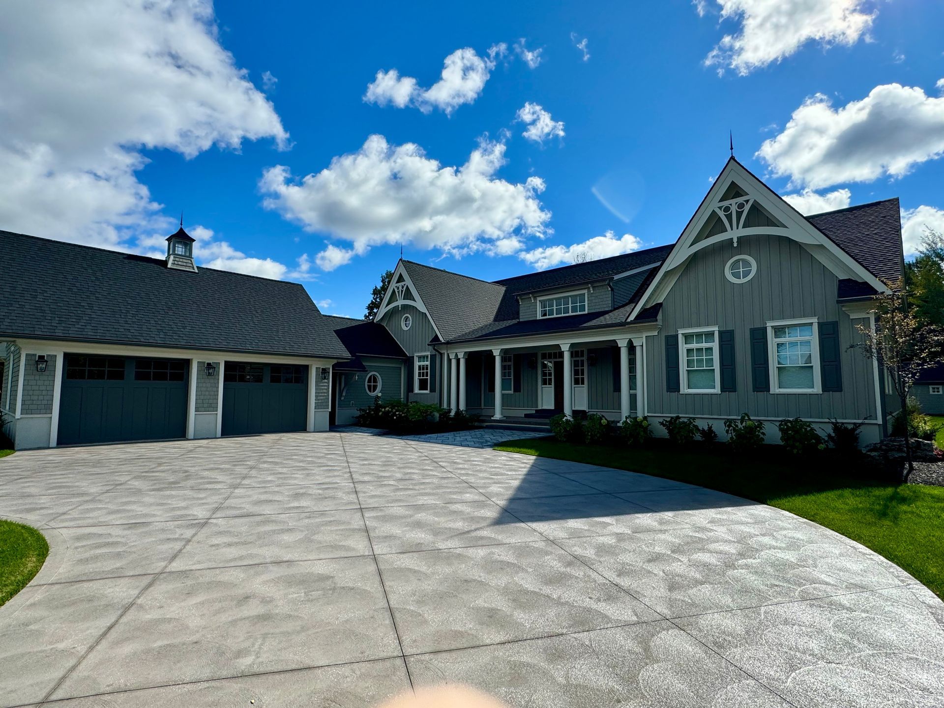 Upscale modern farmhouse with gray siding, a double garage, and a wide concrete driveway under a bright blue sky.