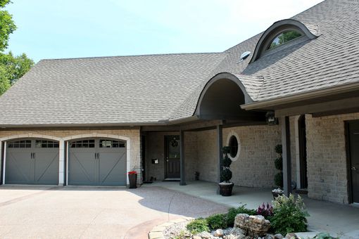 Suburban brick house with double garage, curved dormer window, and arched entryway.