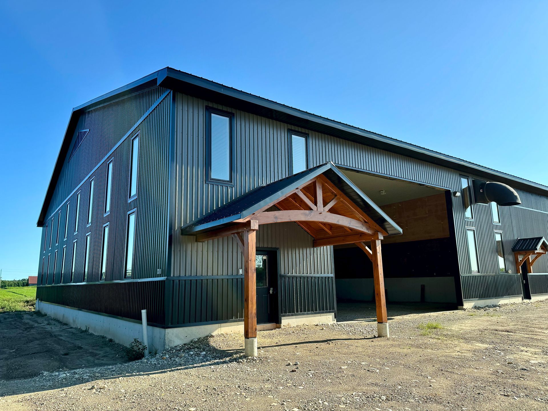 Large metal outbuilding with grey siding and a wooden entrance canopy under a blue sky.
