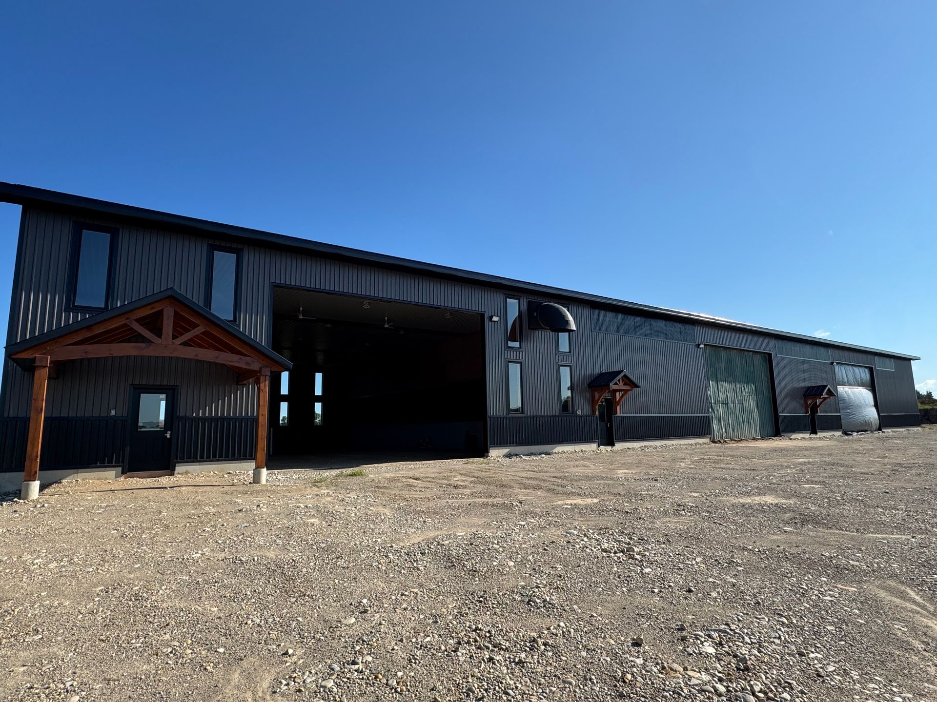 Large metal outbuilding with grey siding and a wooden entrance canopy under a blue sky.