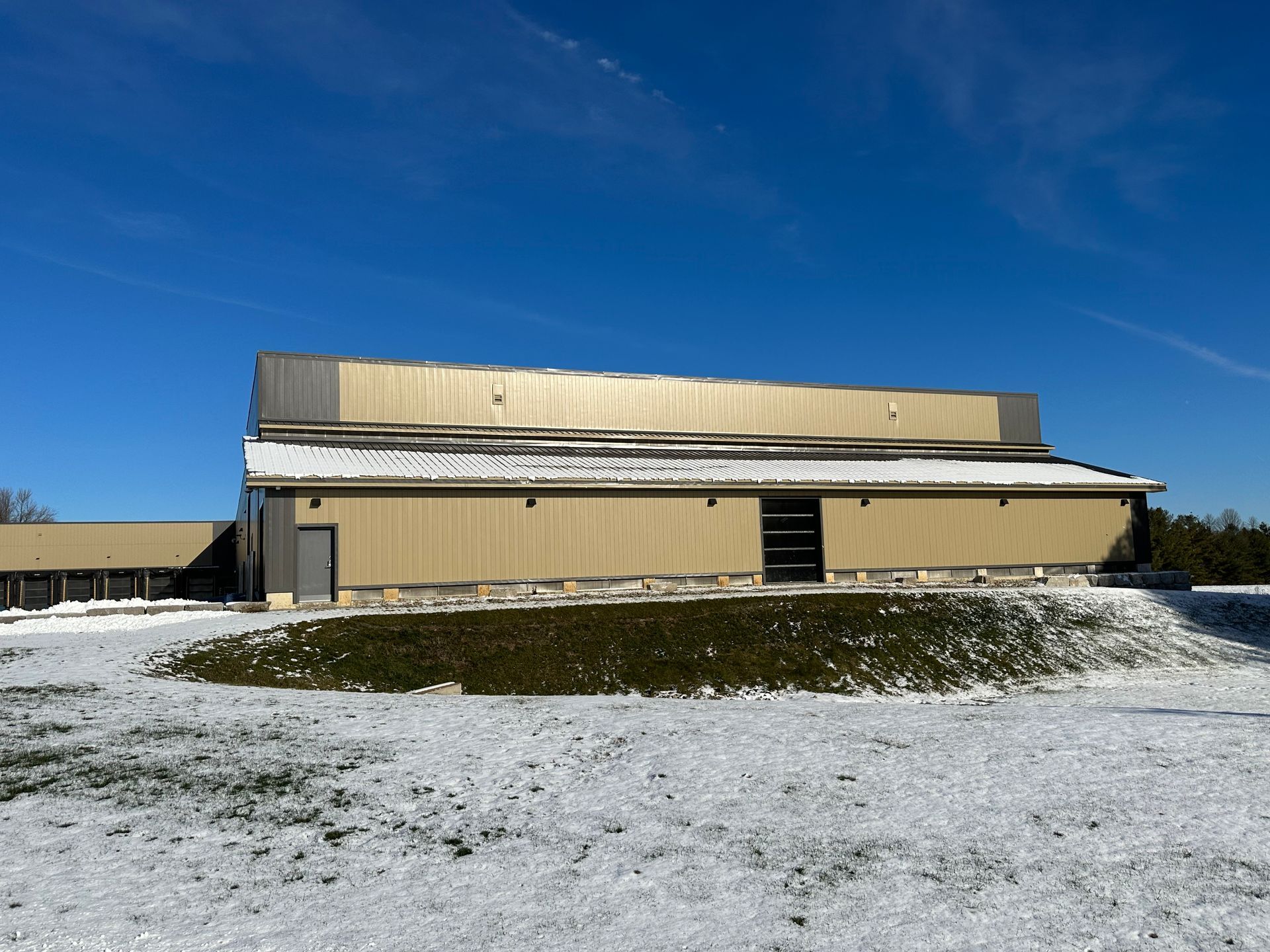 Large beige industrial building with a snow-covered foreground under a clear blue sky