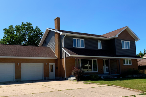 Two-story suburban house showcasing second-story addition with brown and grey siding, brown single roof and a two-car garage.