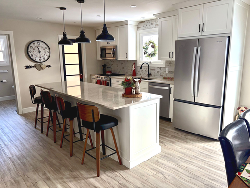 Bright kitchen with white island, black pendant lights, stainless fridge, and wood & black barstools with a light wood floor.