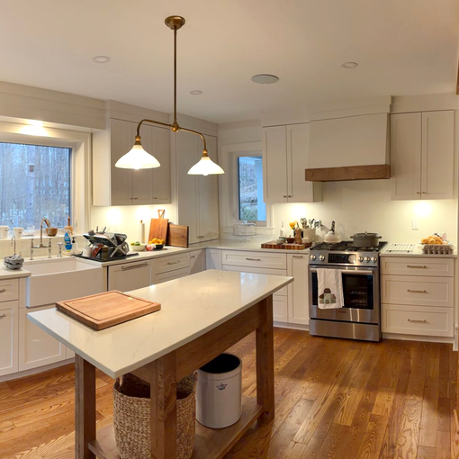 Bright modern kitchen with white cabinets and sink, center island, gold pendant lights, and stainless steel appliances.