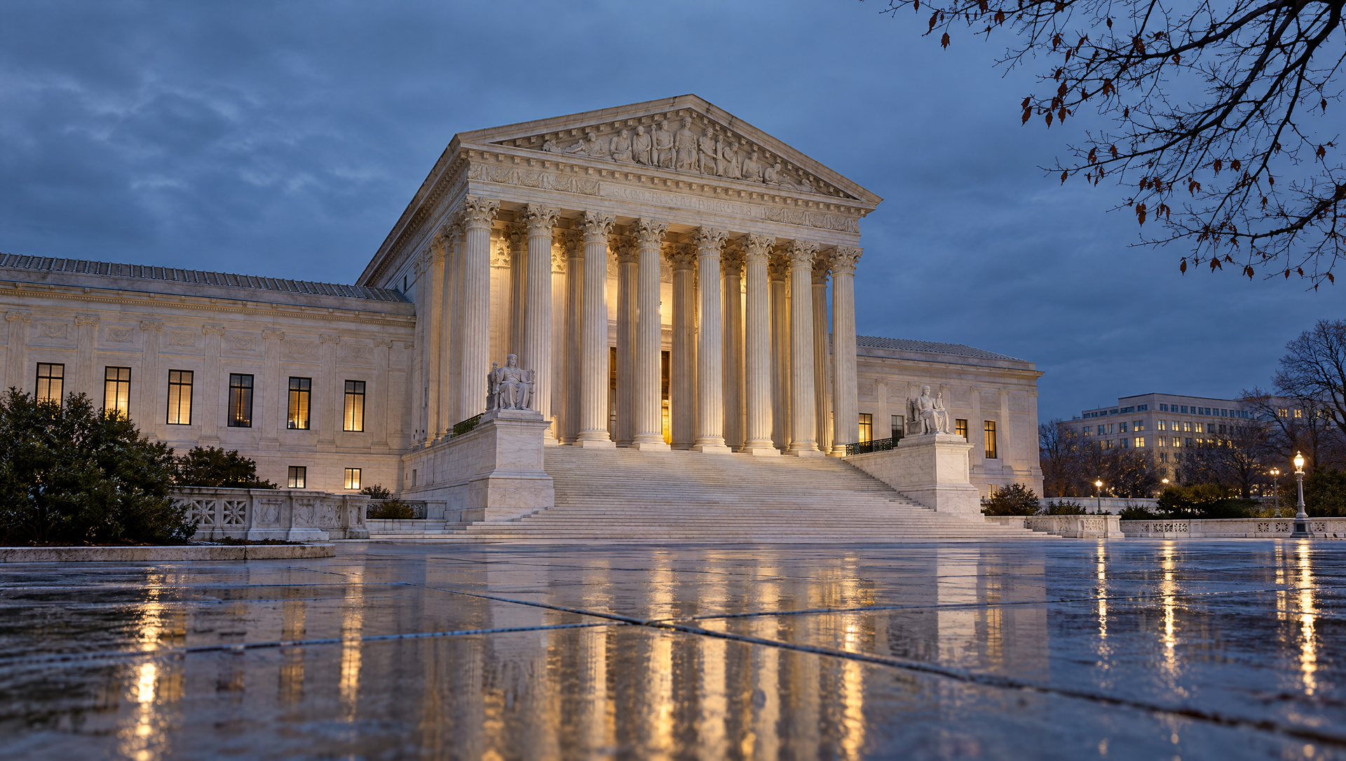 U.S. Supreme Court building lit at dusk, with glowing columns reflected on wet pavement