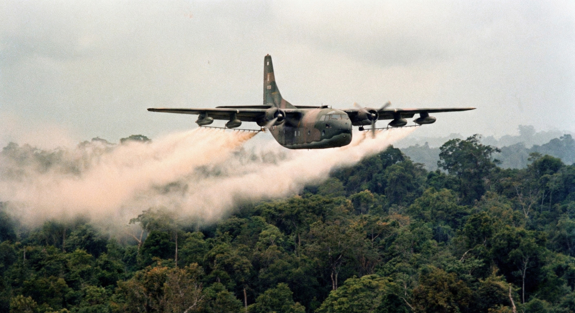 Military cargo plane flying low over a smoky green forest canopy