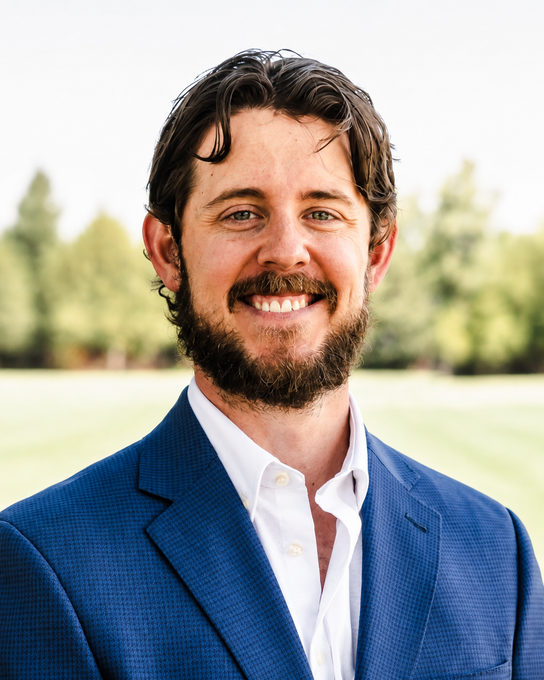 Smiling man in a blue blazer outdoors with blurred trees in the background