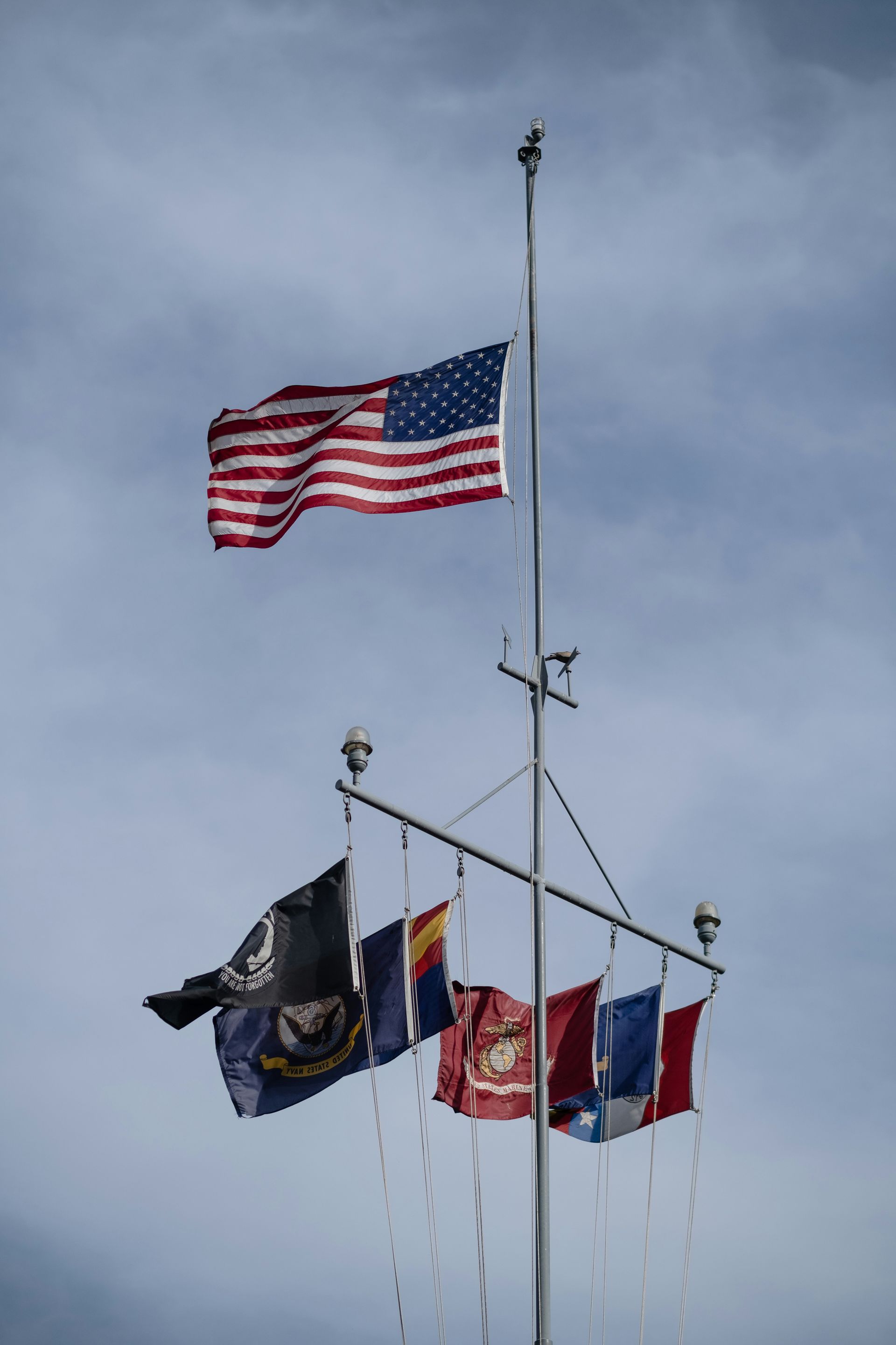 Flags on tall poles waving against a cloudy sky, including a U.S. flag and military-style flags.