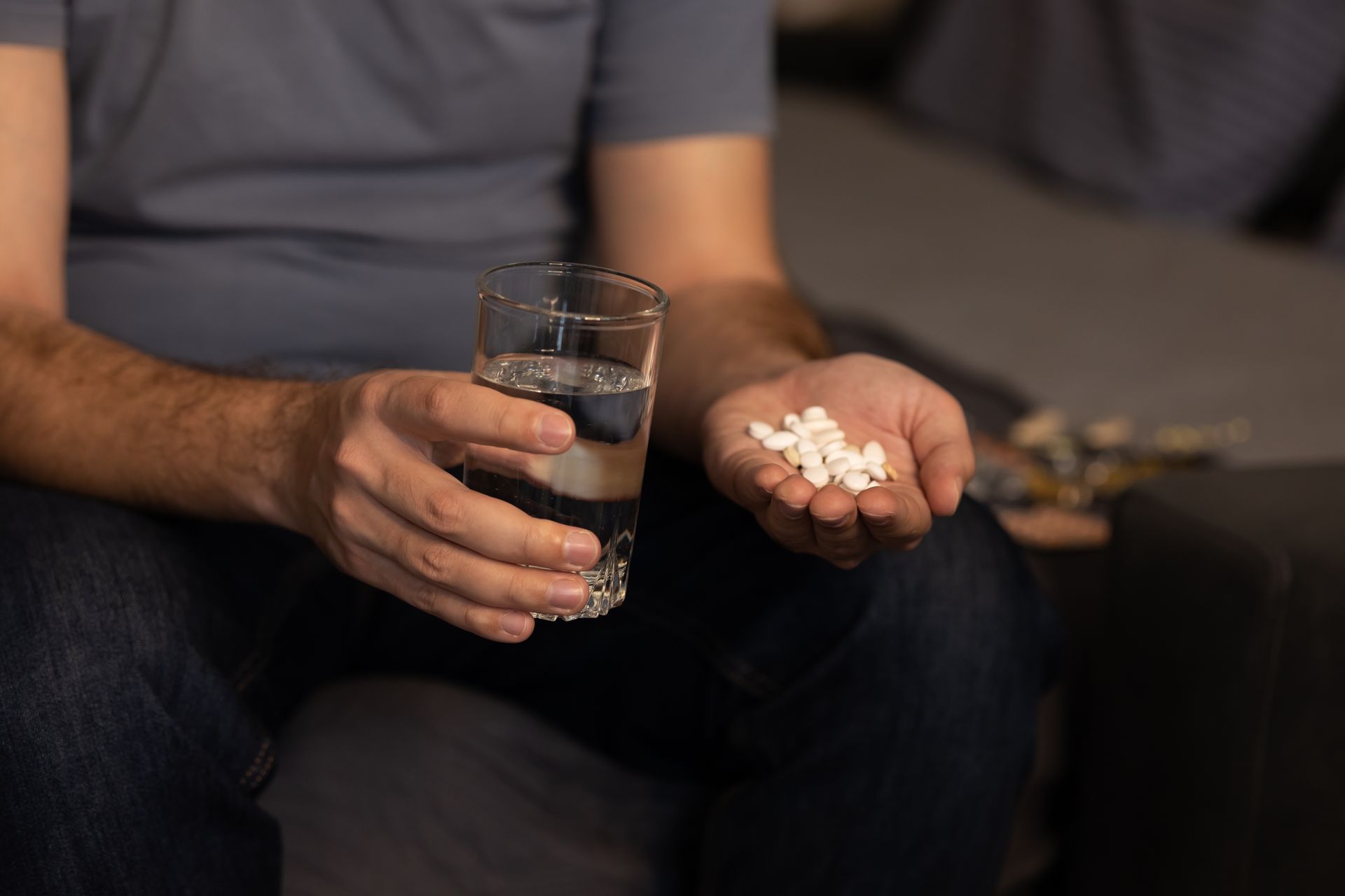 Hand holding a glass of water and white tablets while sitting on a couch