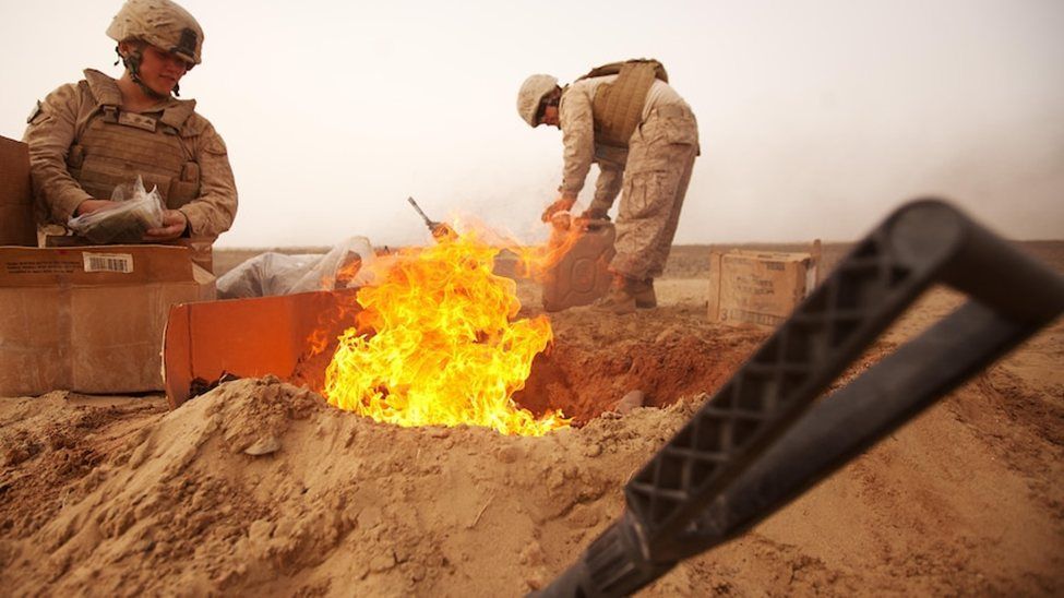 Soldiers tending a fire in a sandy desert trench at dusk