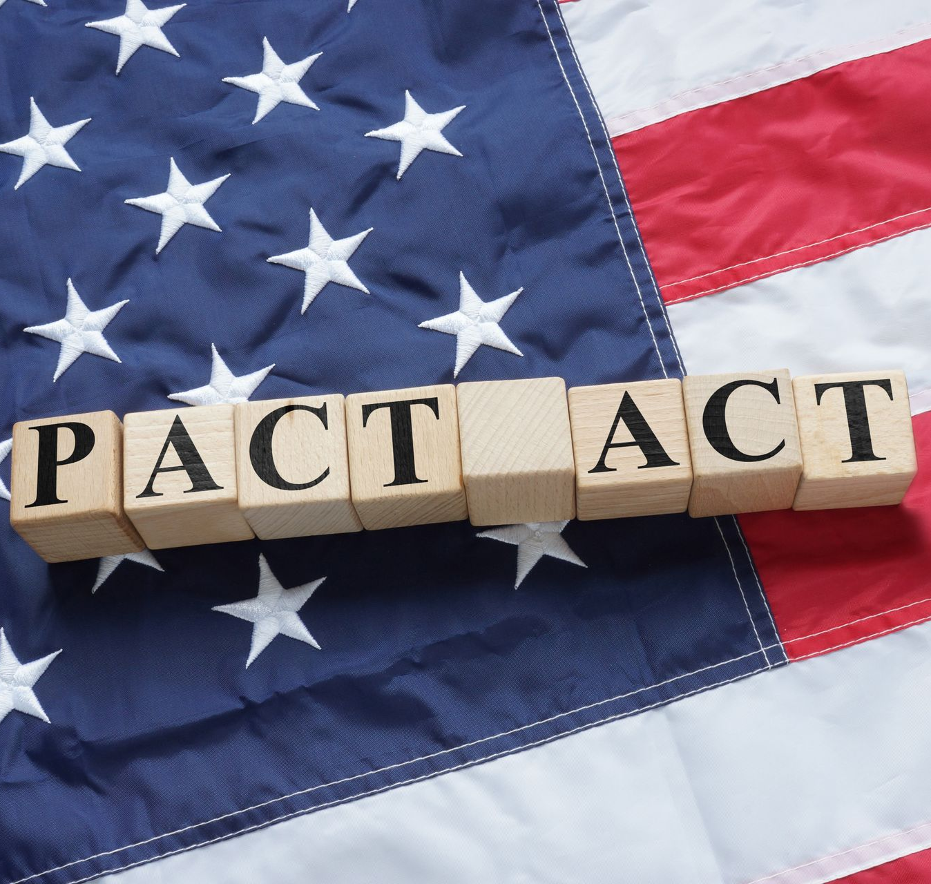 Wooden blocks spelling “PACT ACT” on a U.S. flag background