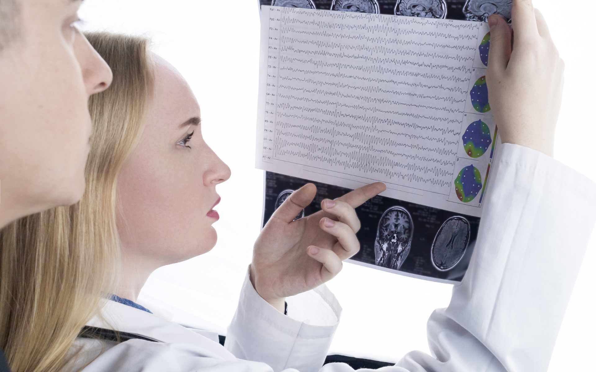 Two doctors reviewing a brain scan and medical chart on a light table.