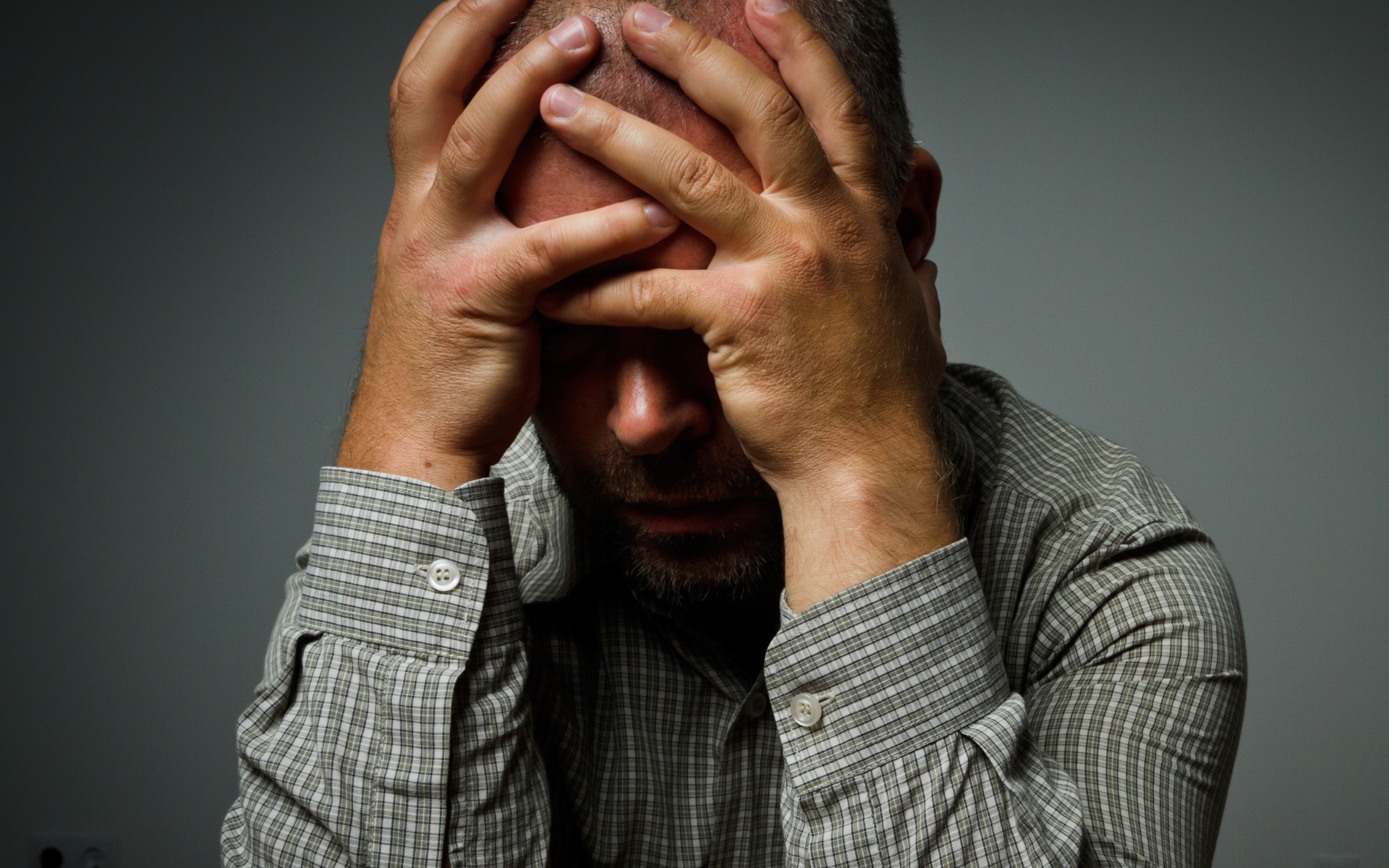Man holding his head in distress, wearing a gray shirt against a dark background