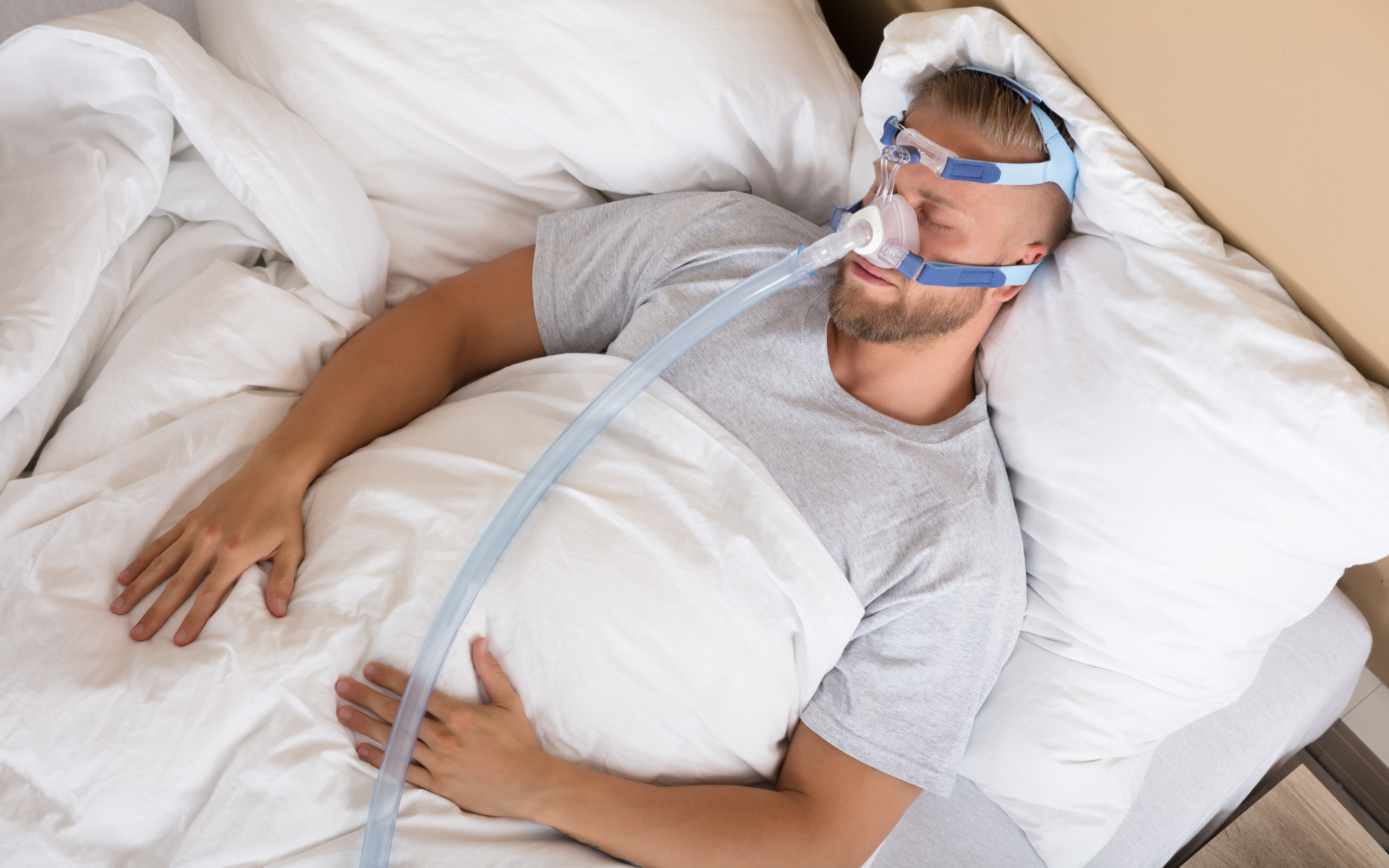 Person lying in bed with a CPAP mask and hose, covered by white bedding
