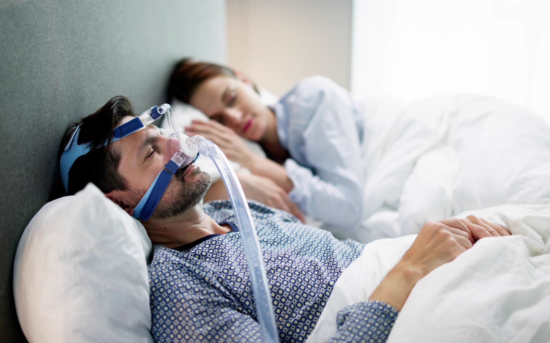 Hospital patient wearing oxygen mask lying in bed while a caregiver rests beside him