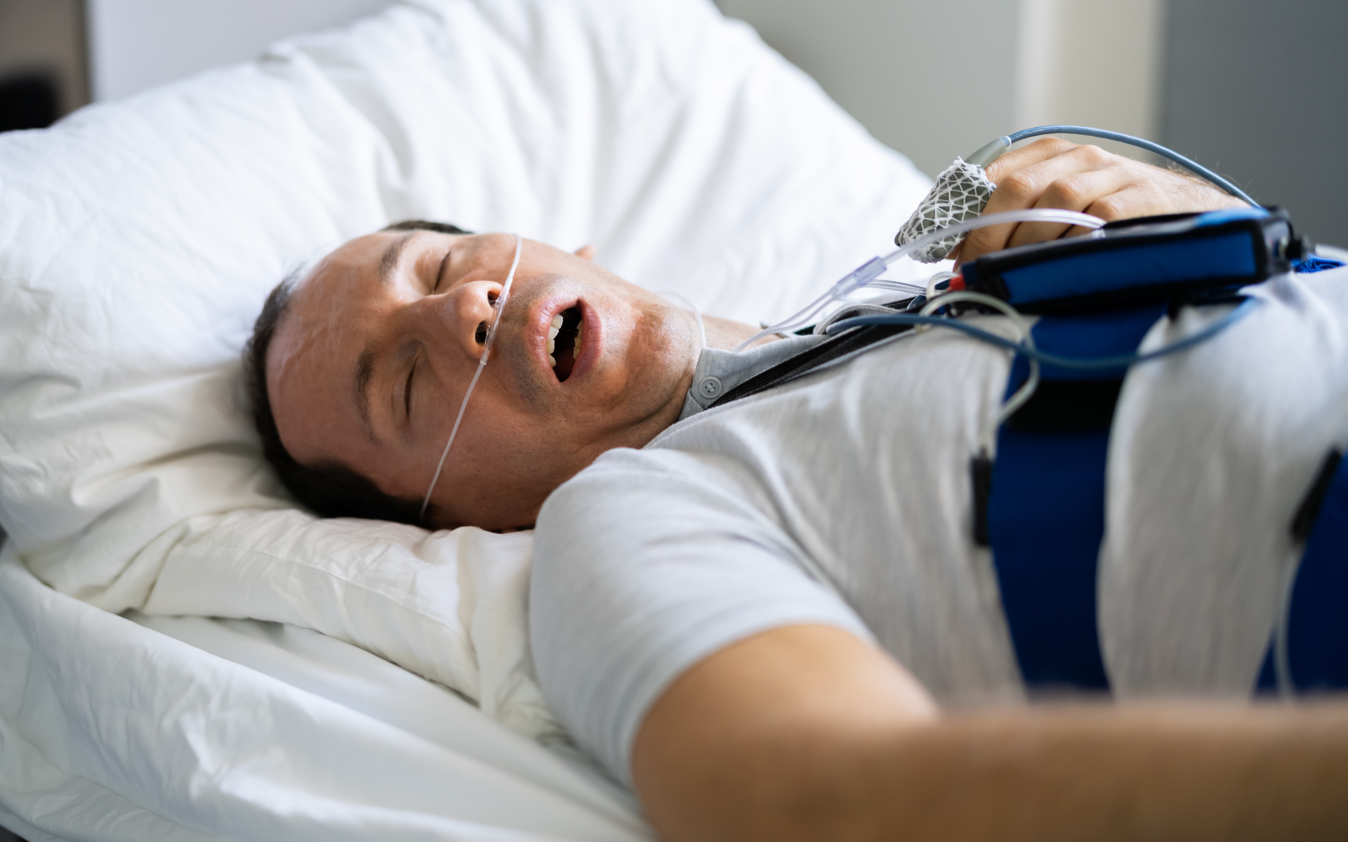 Sleeping patient in hospital bed with breathing mask and chest monitor belts