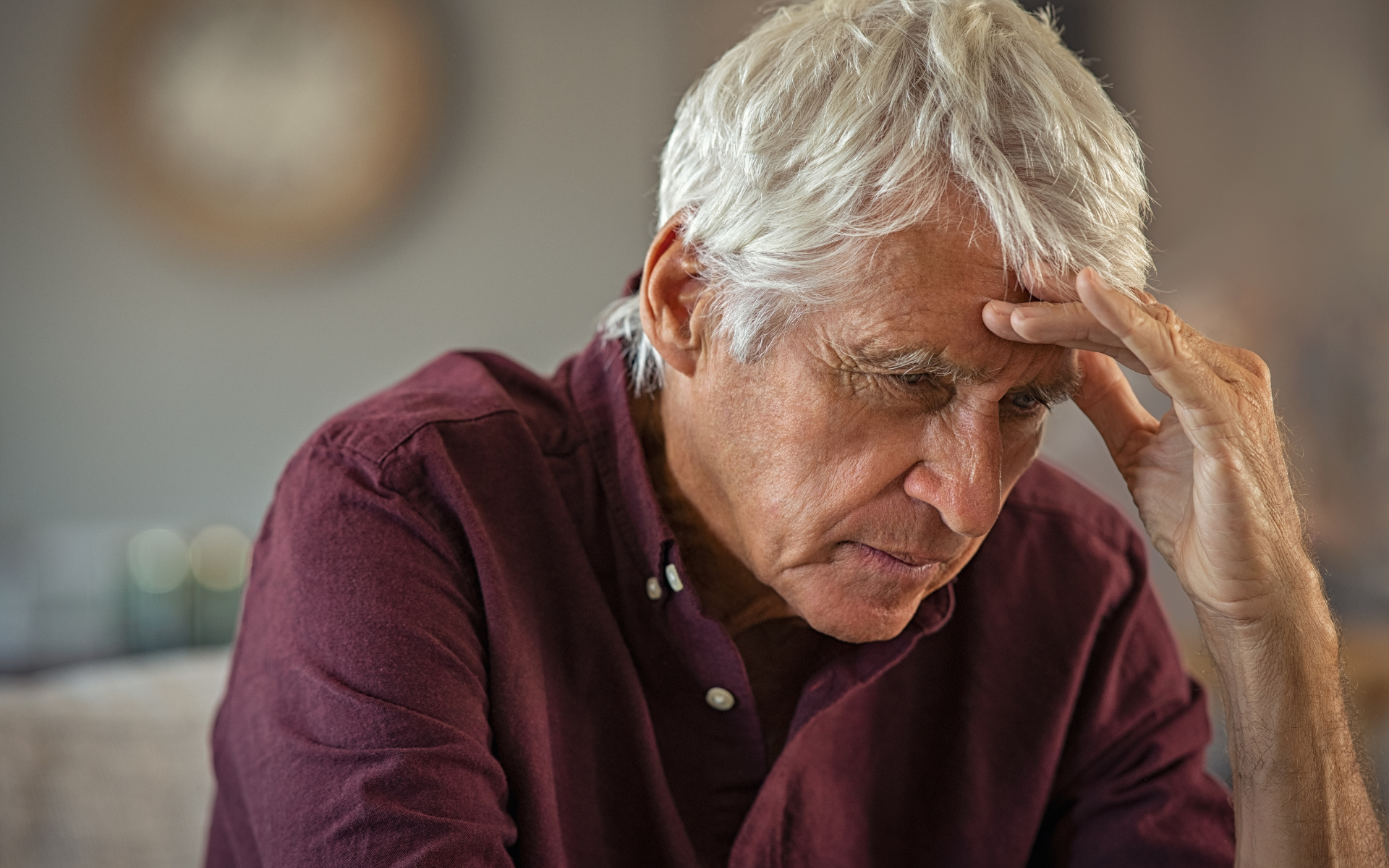 Man holding his forehead with eyes closed, looking distressed at a table indoors.