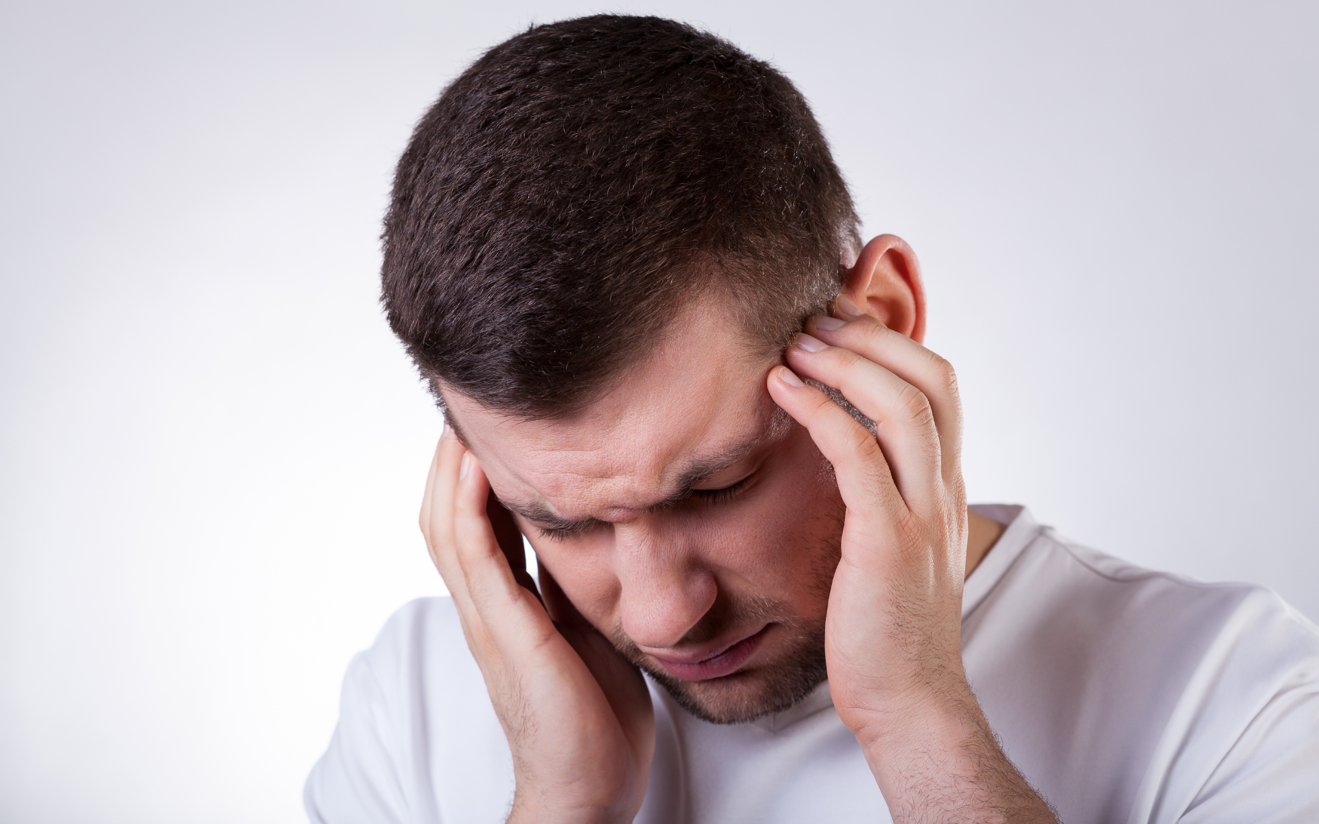Man holding his temples with eyes closed, looking stressed against a plain background