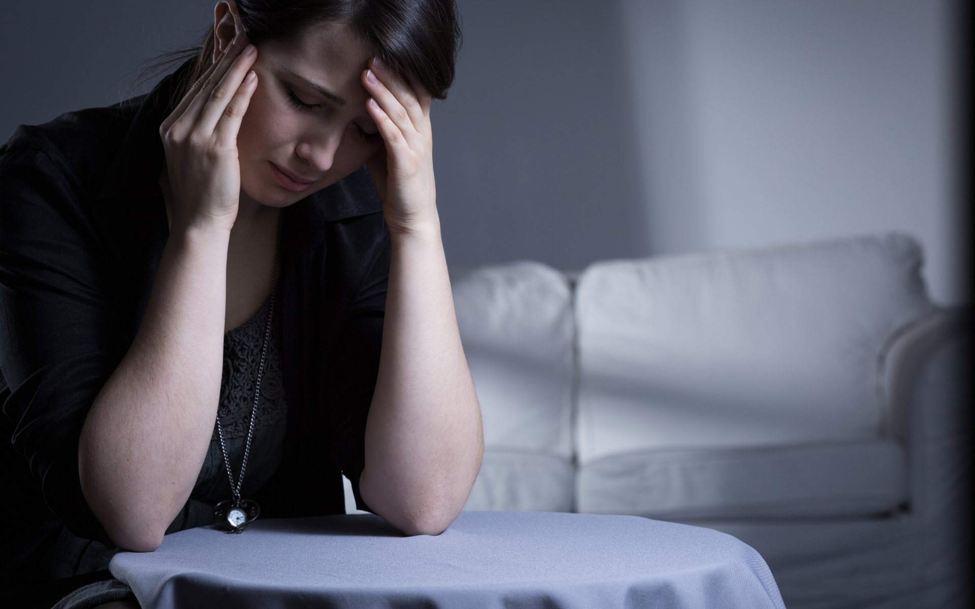 Woman sitting on a couch, holding her head with a distressed expression.