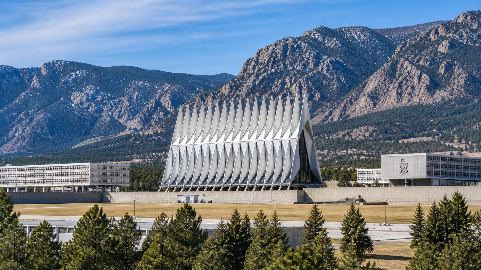 Modern white building with sculptural spires in front of mountains and trees under a clear sky