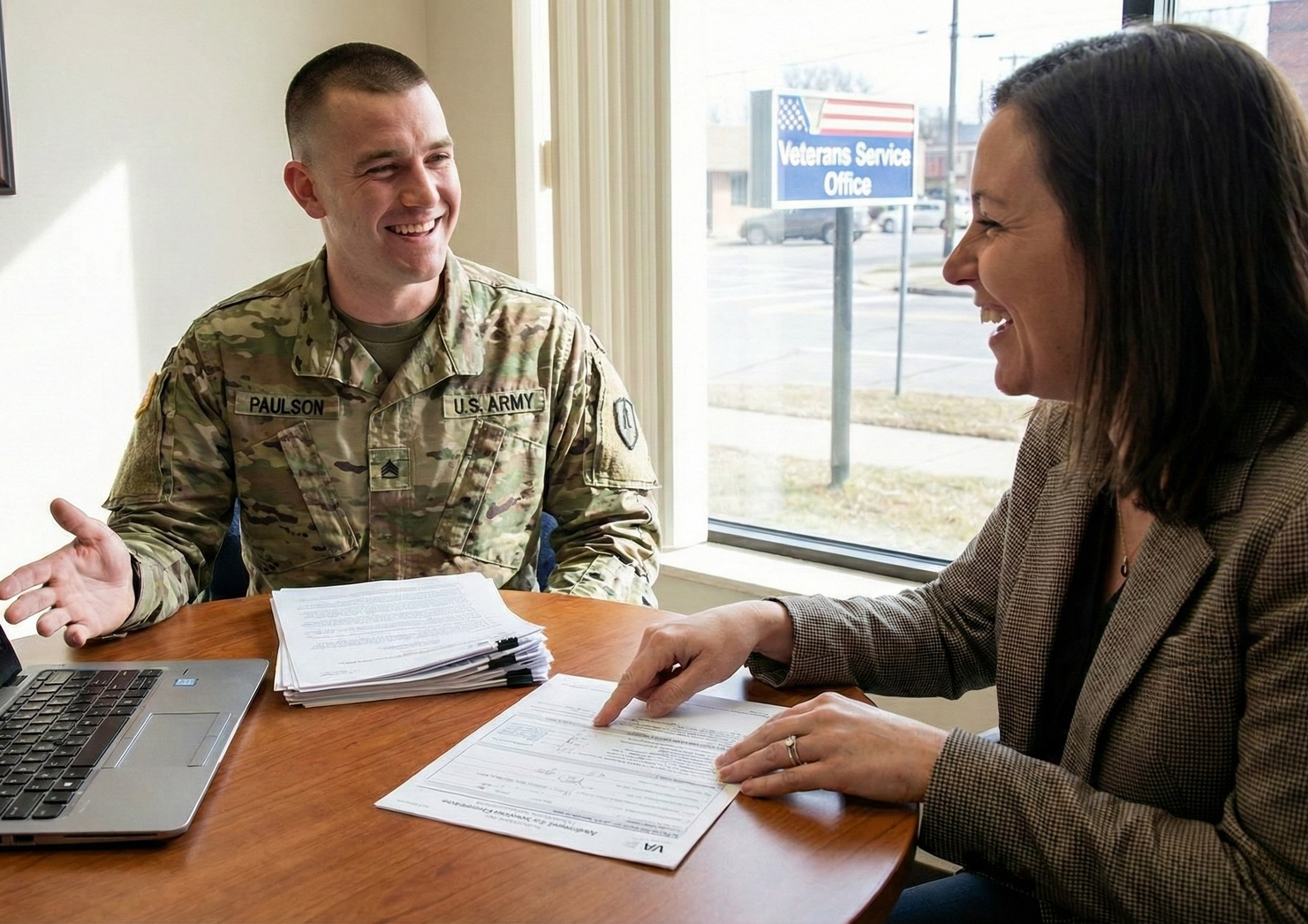 Soldier and woman smiling across a table, reviewing paperwork near a window