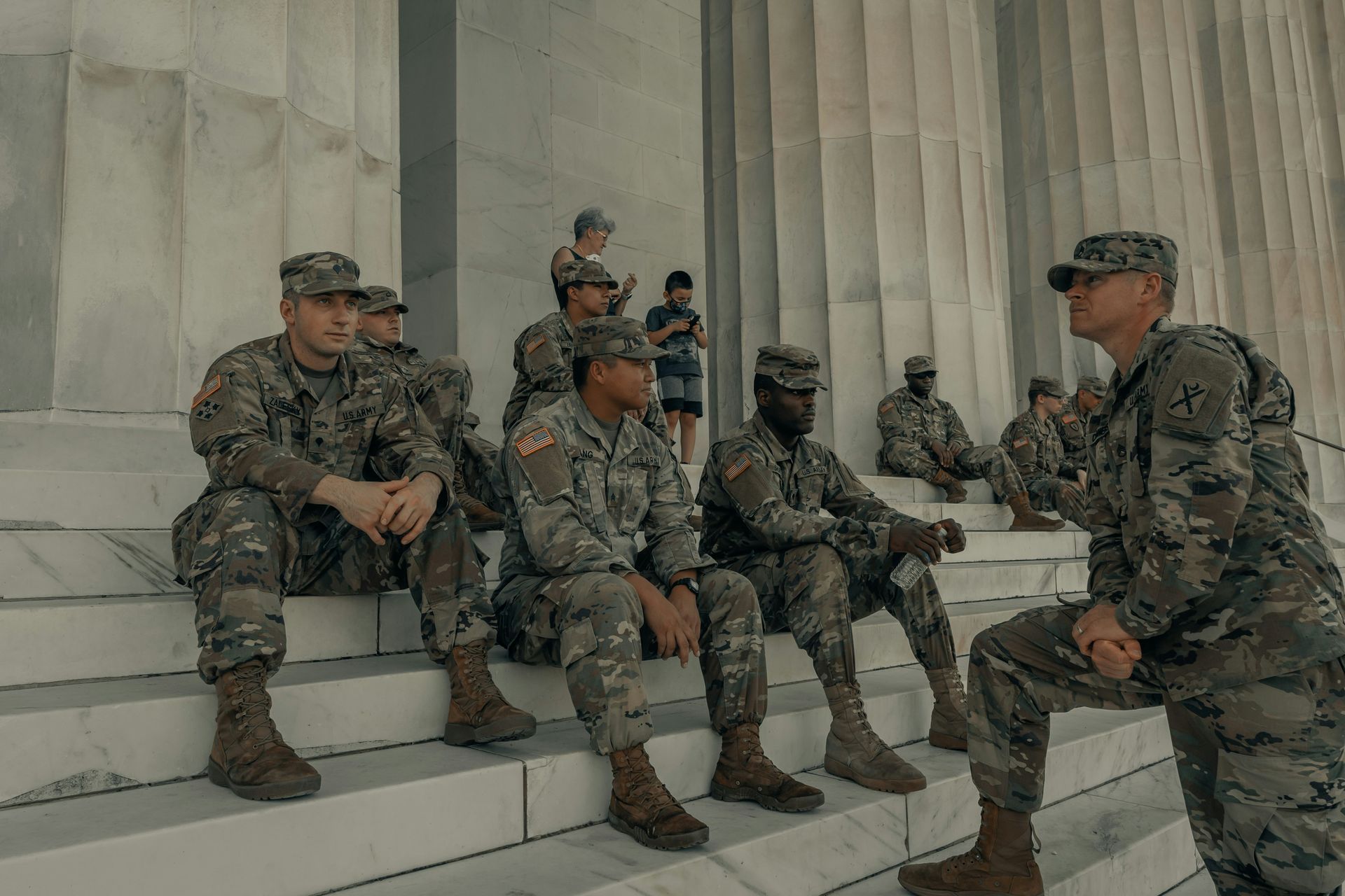 Soldiers in camouflage uniforms sitting and standing on marble steps outside a monumental building