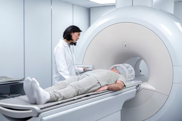 Patient on MRI scanner table with technician beside the machine in a clinical room