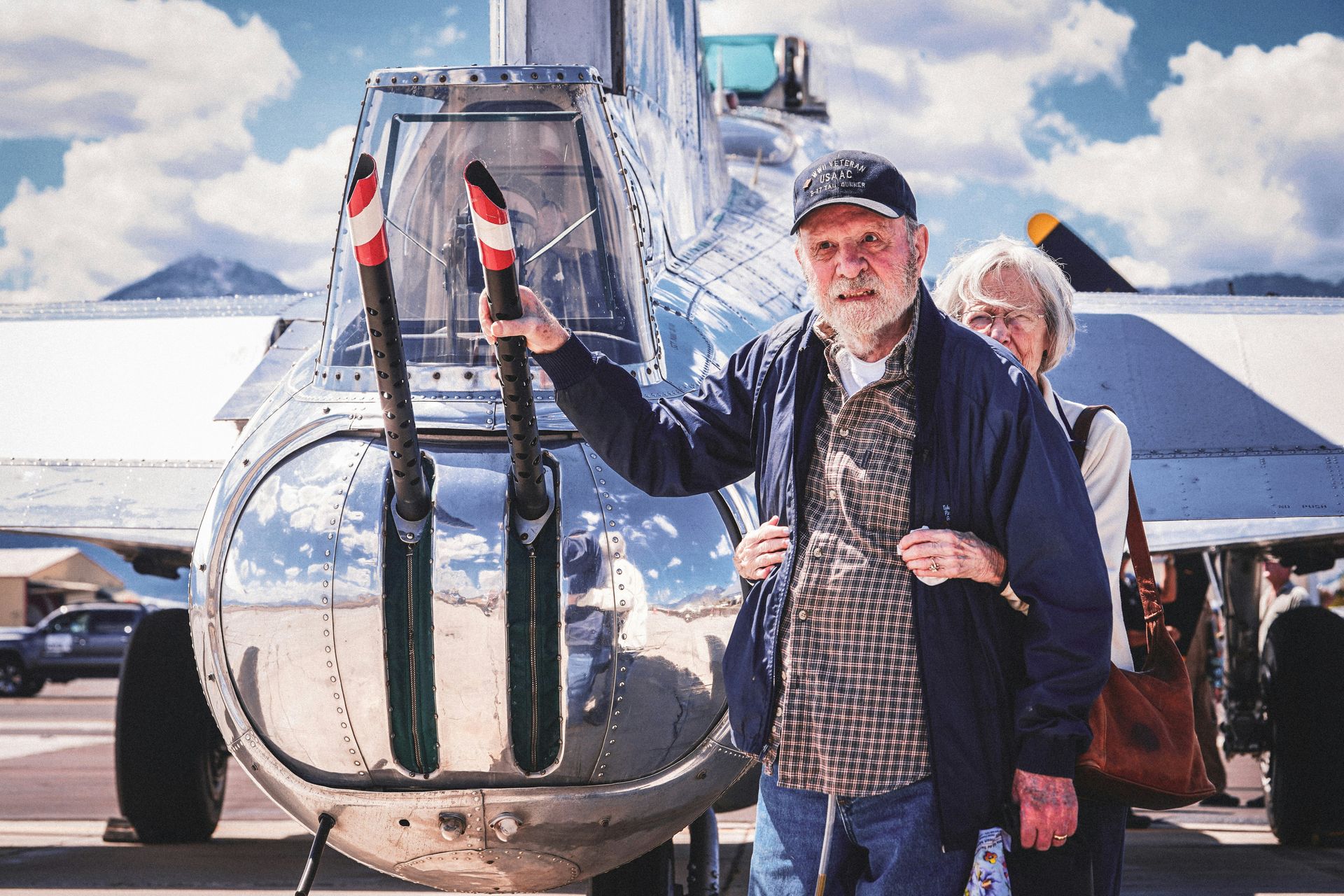 Man standing by a helicopter, holding a red-and-white object, with another person behind him on a tarmac.