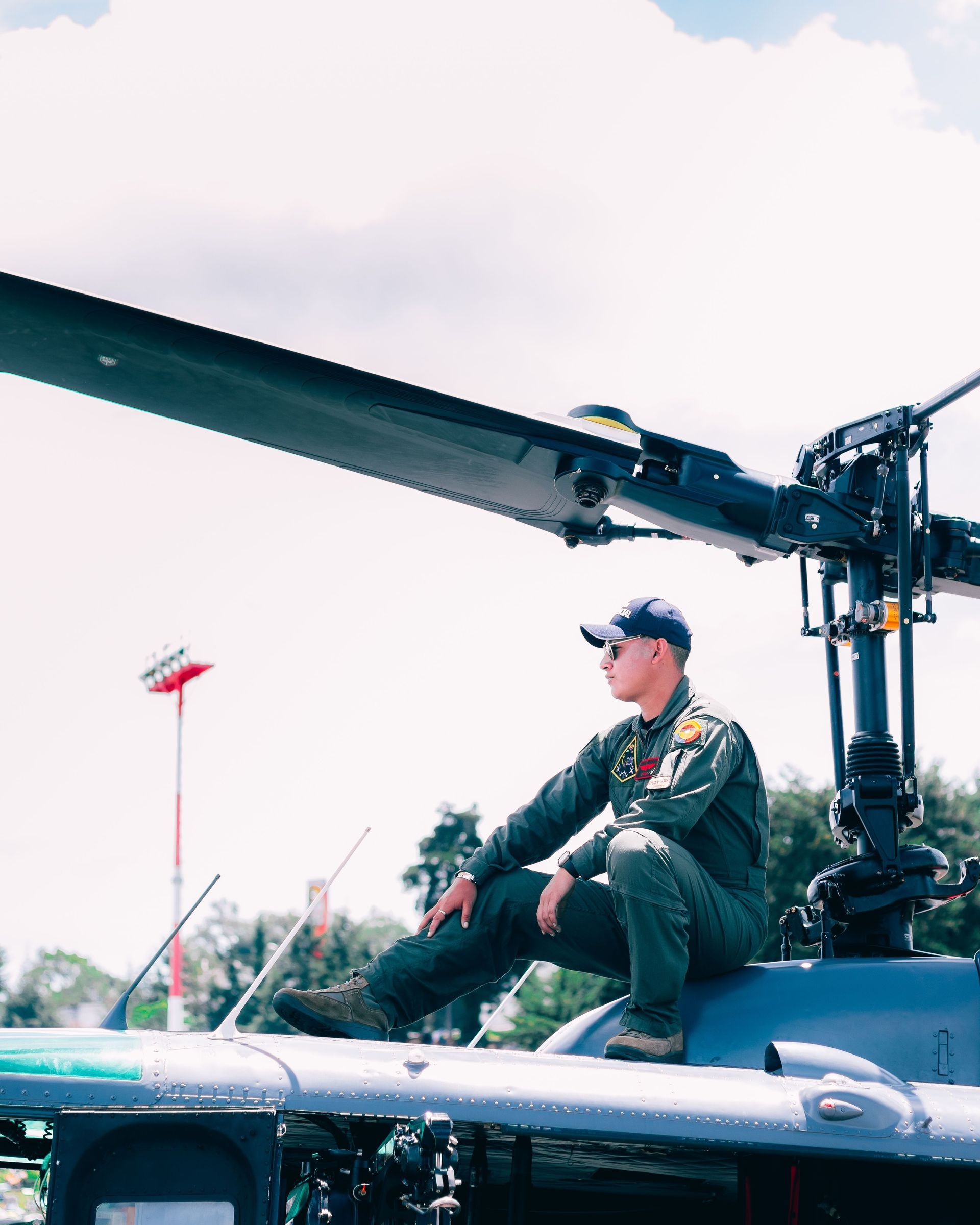 Soldier in camouflage sits on a bed, head bowed, in a dim room near a window.