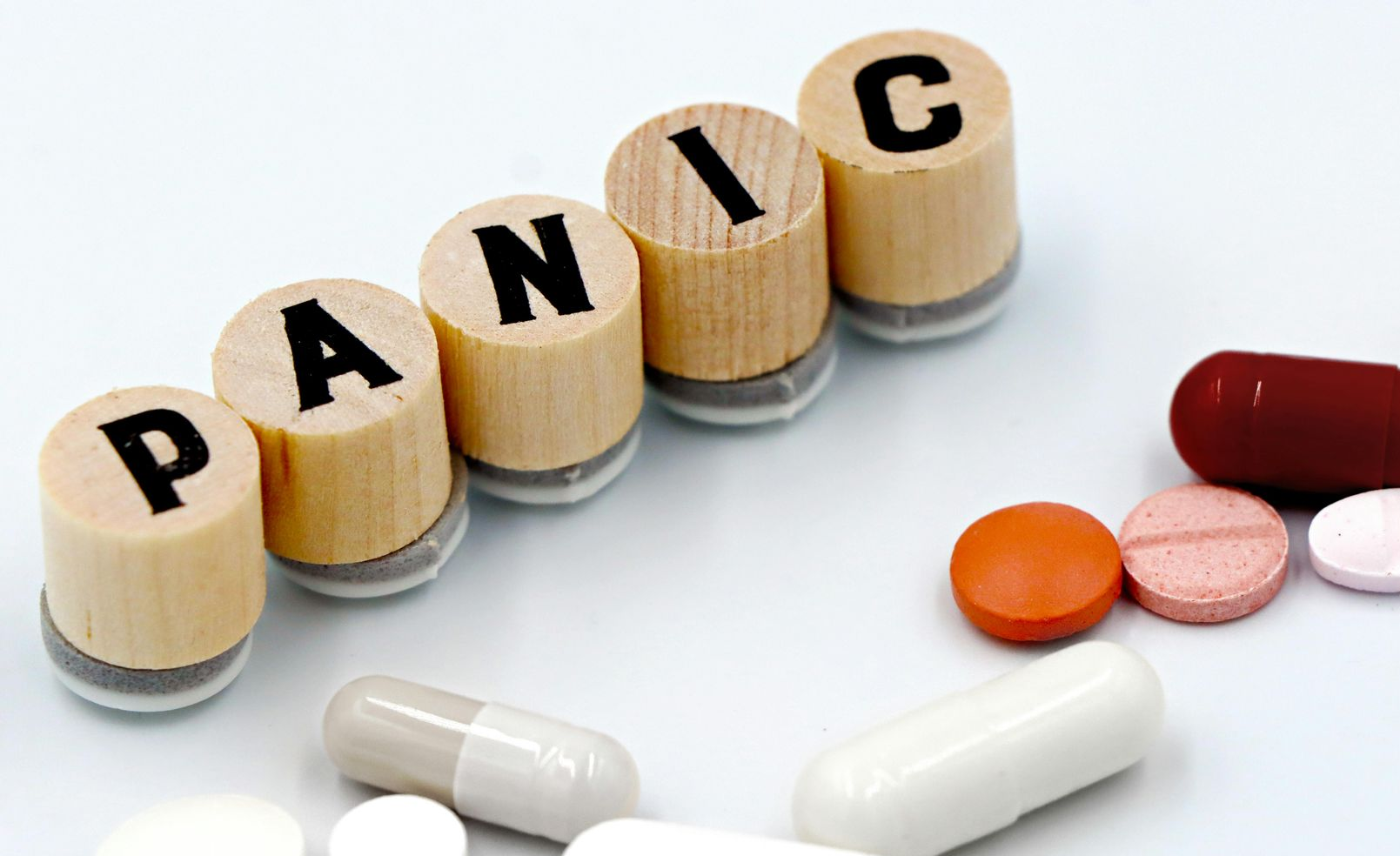 Wooden letter blocks spelling “PANIC” beside assorted pills and capsules on a white surface