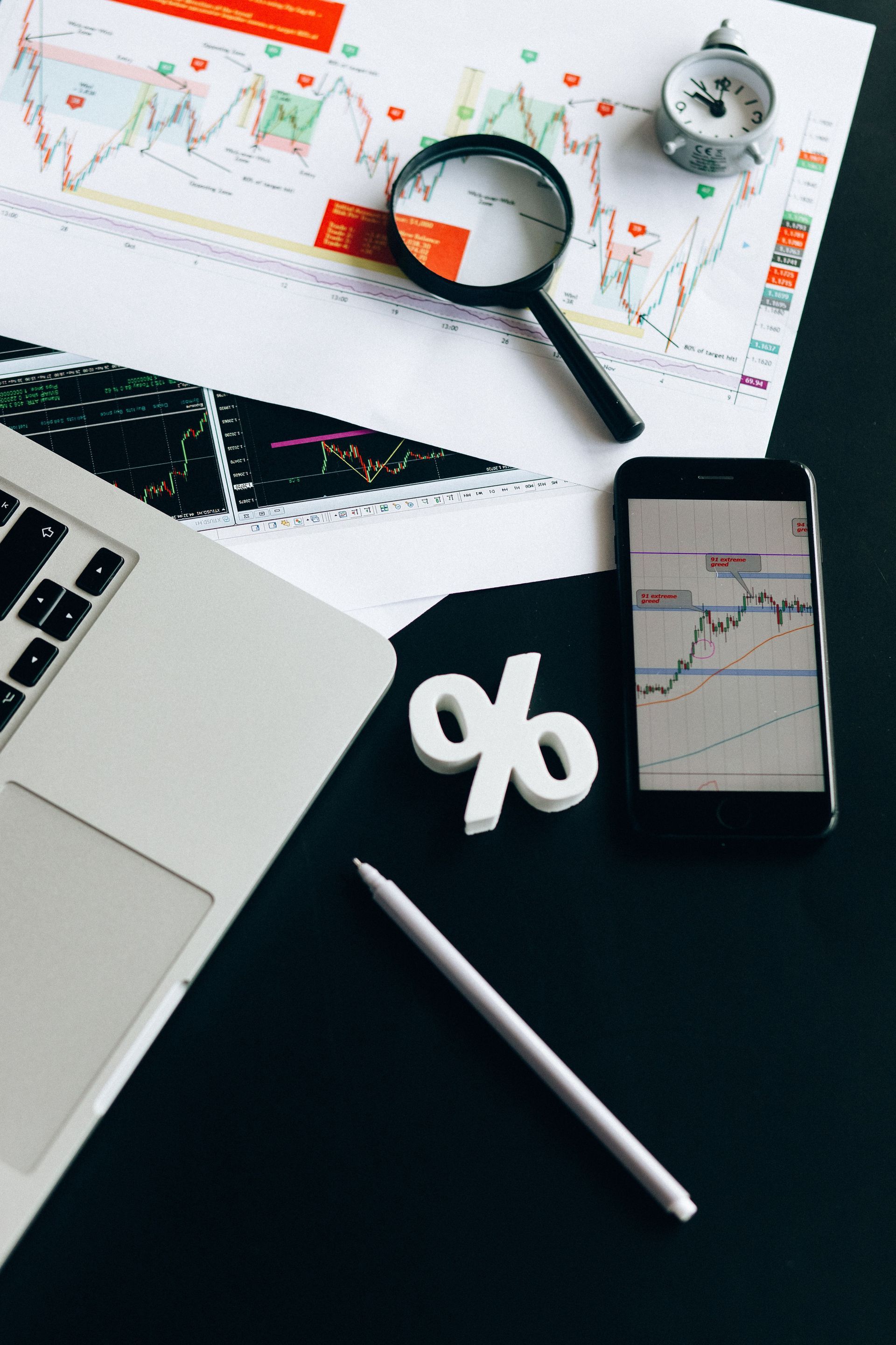 Marketing workspace with laptop, charts, phone, magnifying glass, and white percent sign on a dark desk