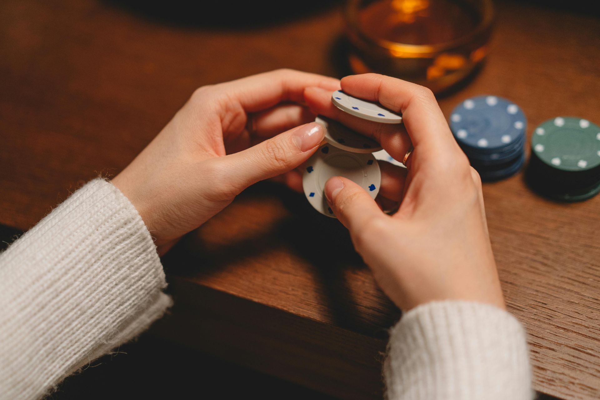 Hands holding a small stacked device on a wooden table, with colorful round objects and a glass in the background