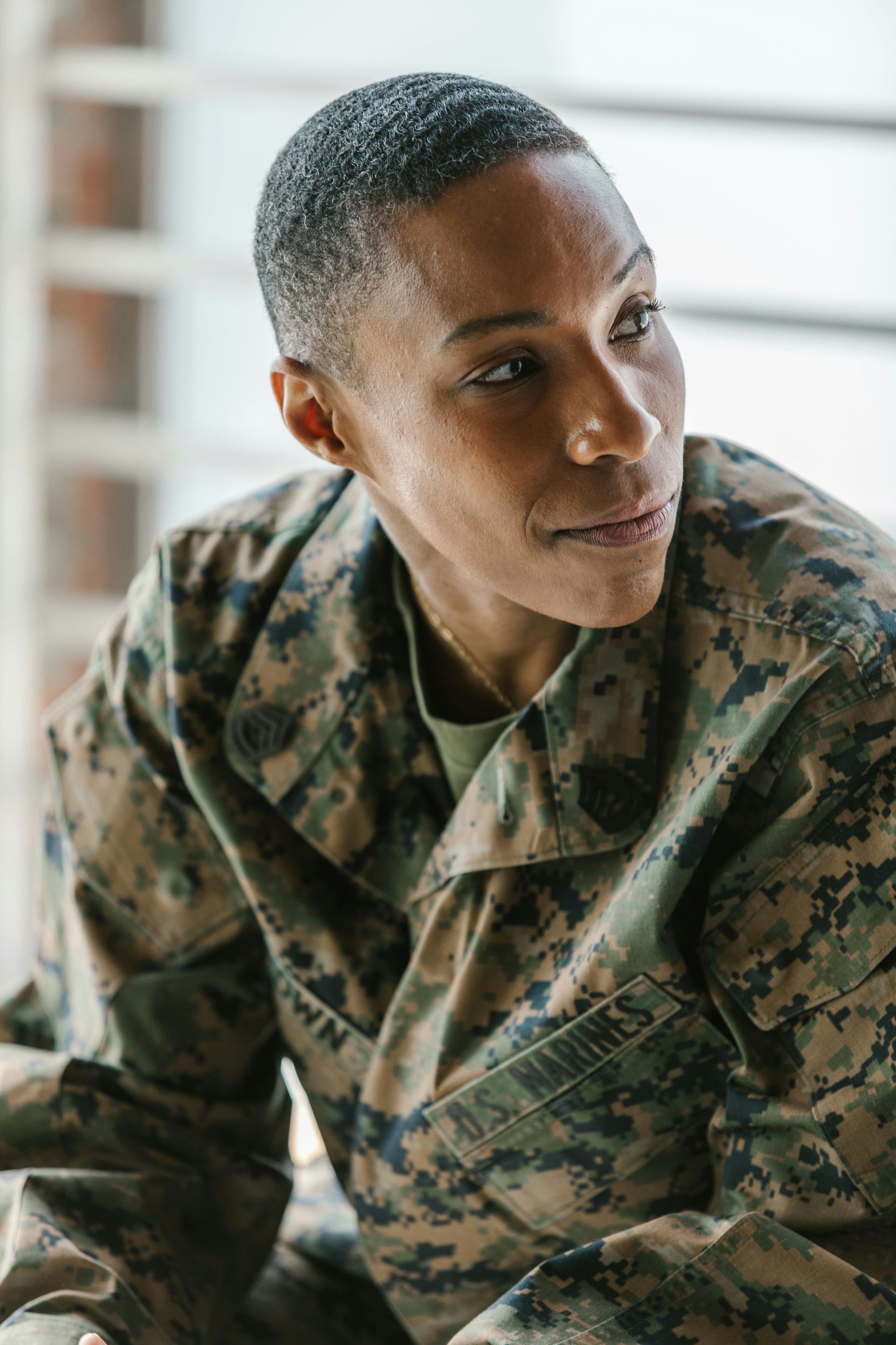 Person in camouflage jacket looking to the side by a bright window