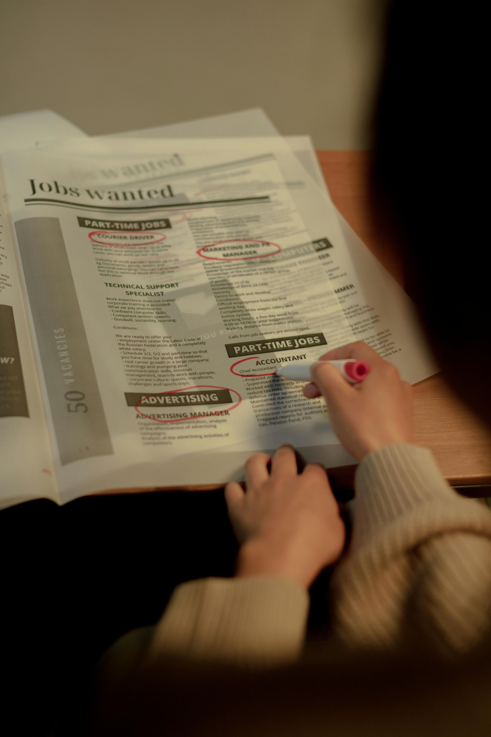 Person reading a newspaper at a table, with a hand holding the page and another resting on the paper.