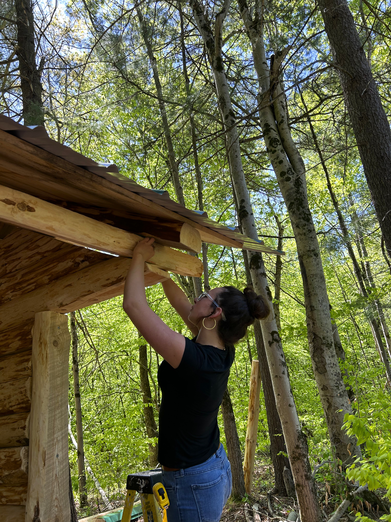 Person reaching up to adjust a wooden roof edge on lean-to.