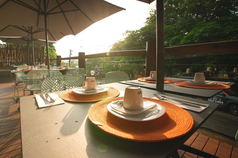 Uma mesa com pratos e xícaras sob um guarda-chuva Pousada Xica