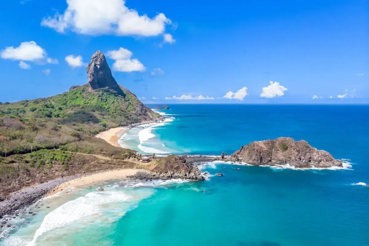 Uma vista aérea de uma praia com uma montanha ao fundo e um grande corpo de água Pousada Xica