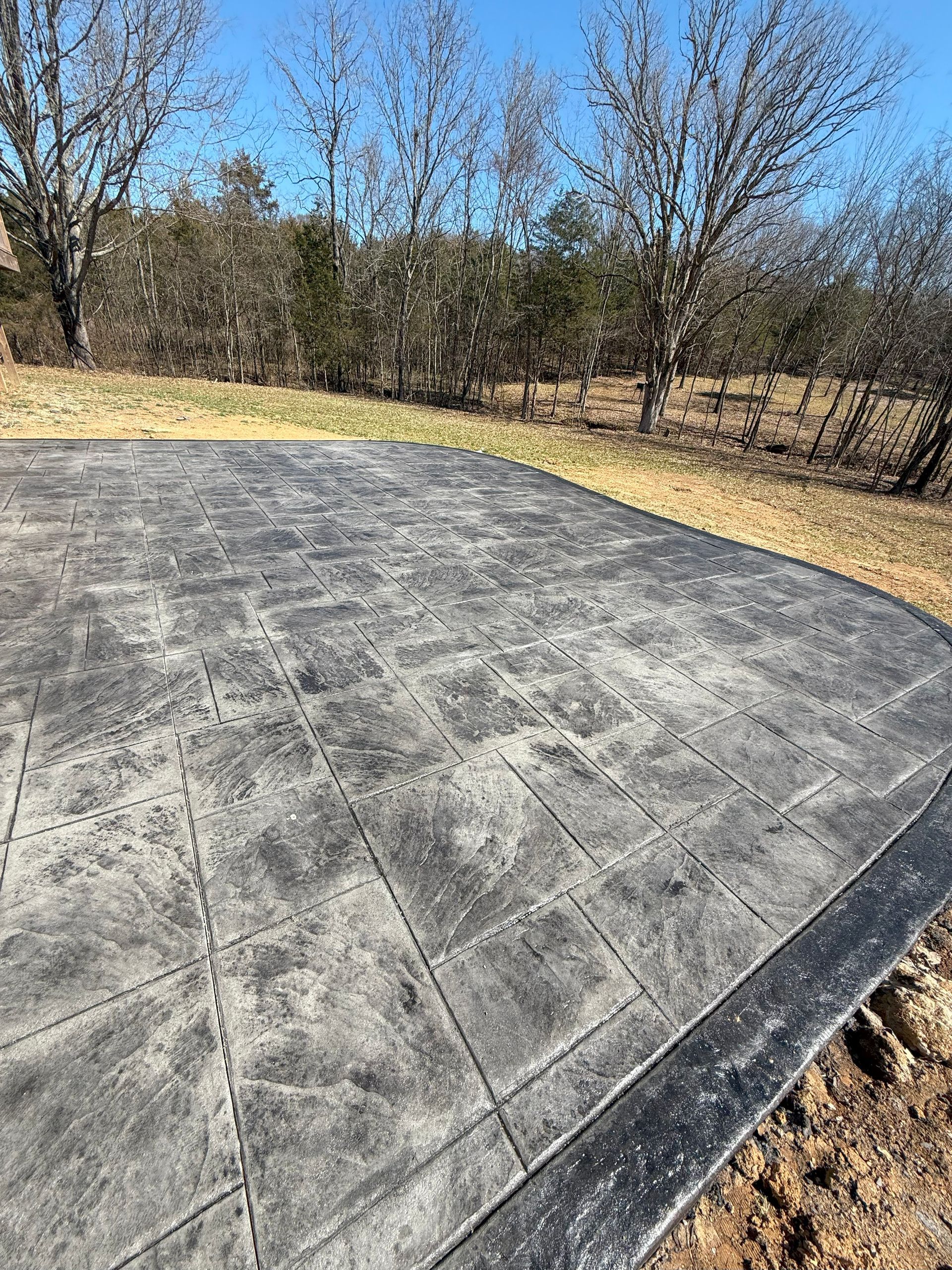 A concrete driveway with a black border and trees in the background.