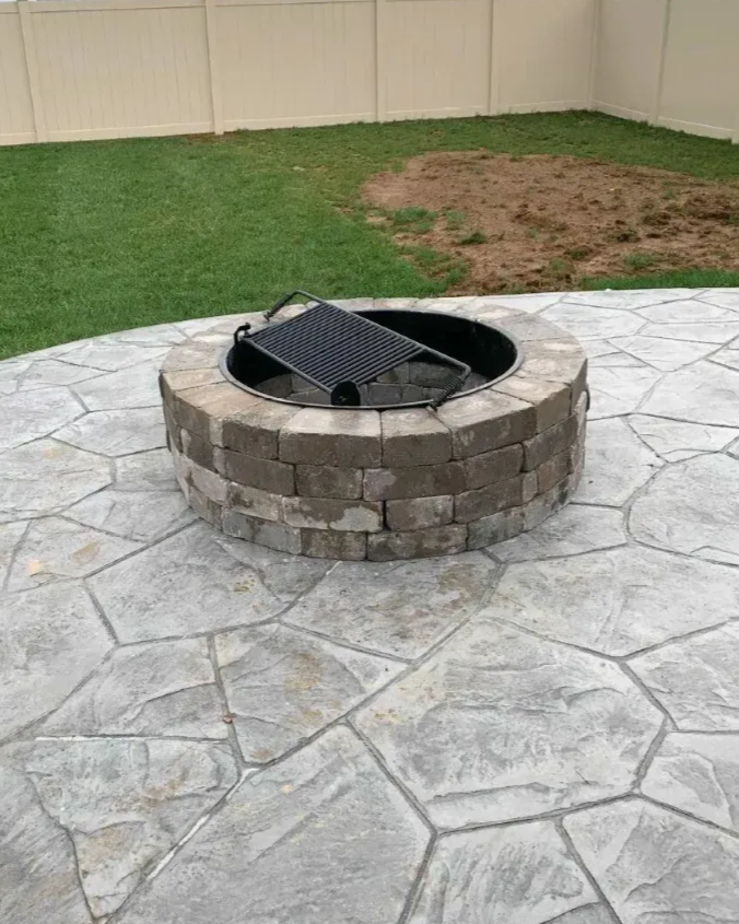 Stone fire pit on a stamped concrete patio with grass and a dirt patch in the background