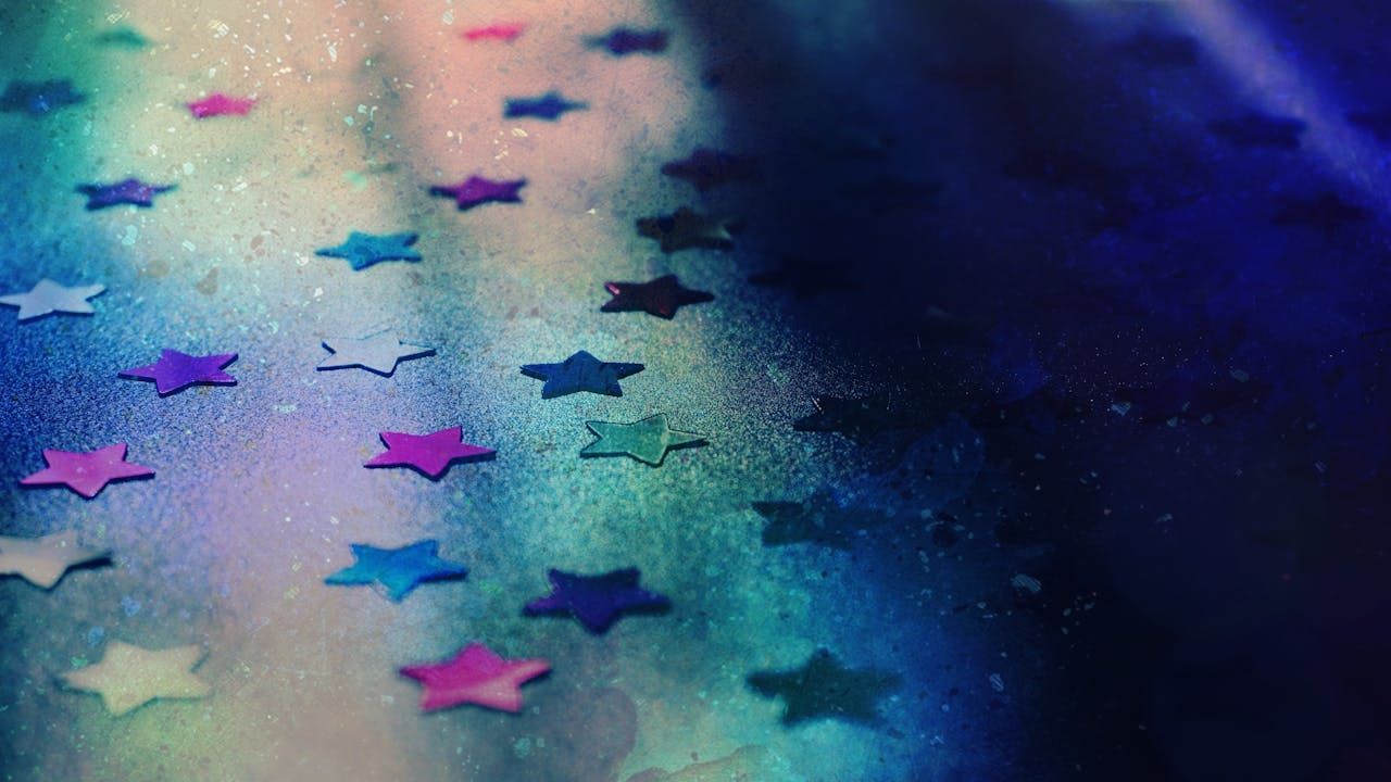 Colorful star-shaped confetti scattered on a gradient blue and purple background with a soft, dreamy texture.