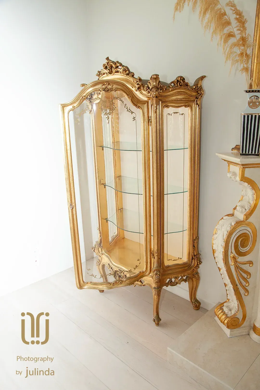 Ornate 24k gold display cabinet in a bright white room, next to a white and gold fireplace. By Julinda at Total Creativeyphotography.
