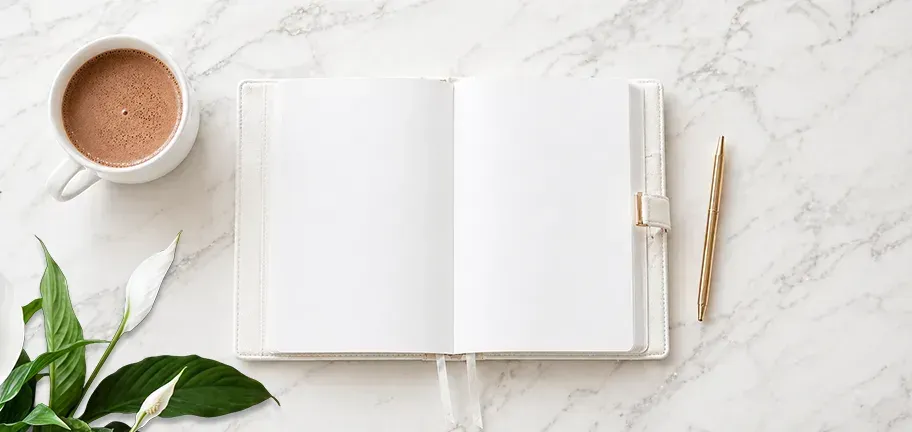 Open diary on white marble desk with coffee cup, gold pen. Total Creative Starting A Business Guide