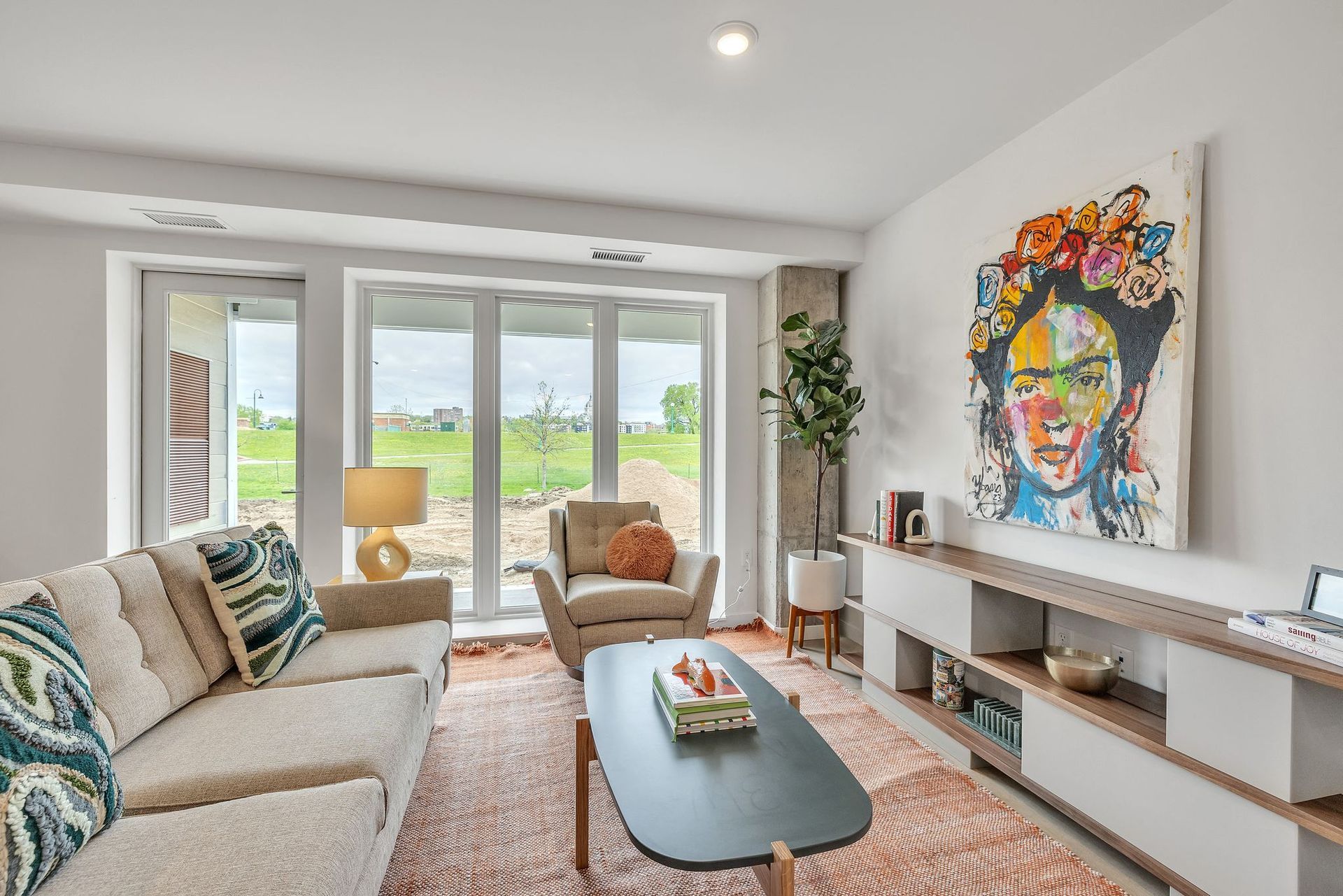 Living room with colorful art, couch, armchair, rug, and view of the outdoors through sliding glass doors.