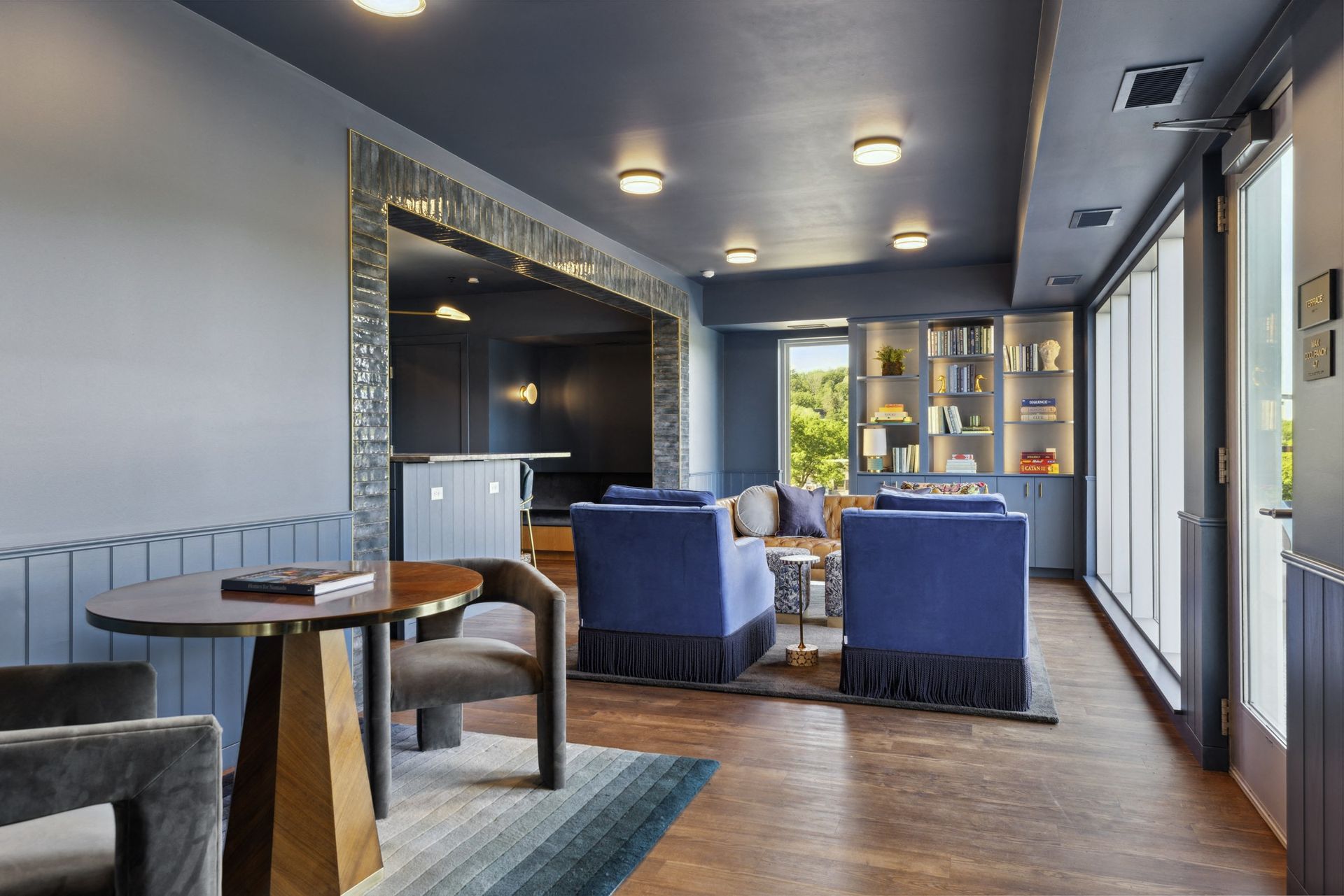 Lounge with blue walls and furniture, a round table, and a built-in bookcase near large windows.
