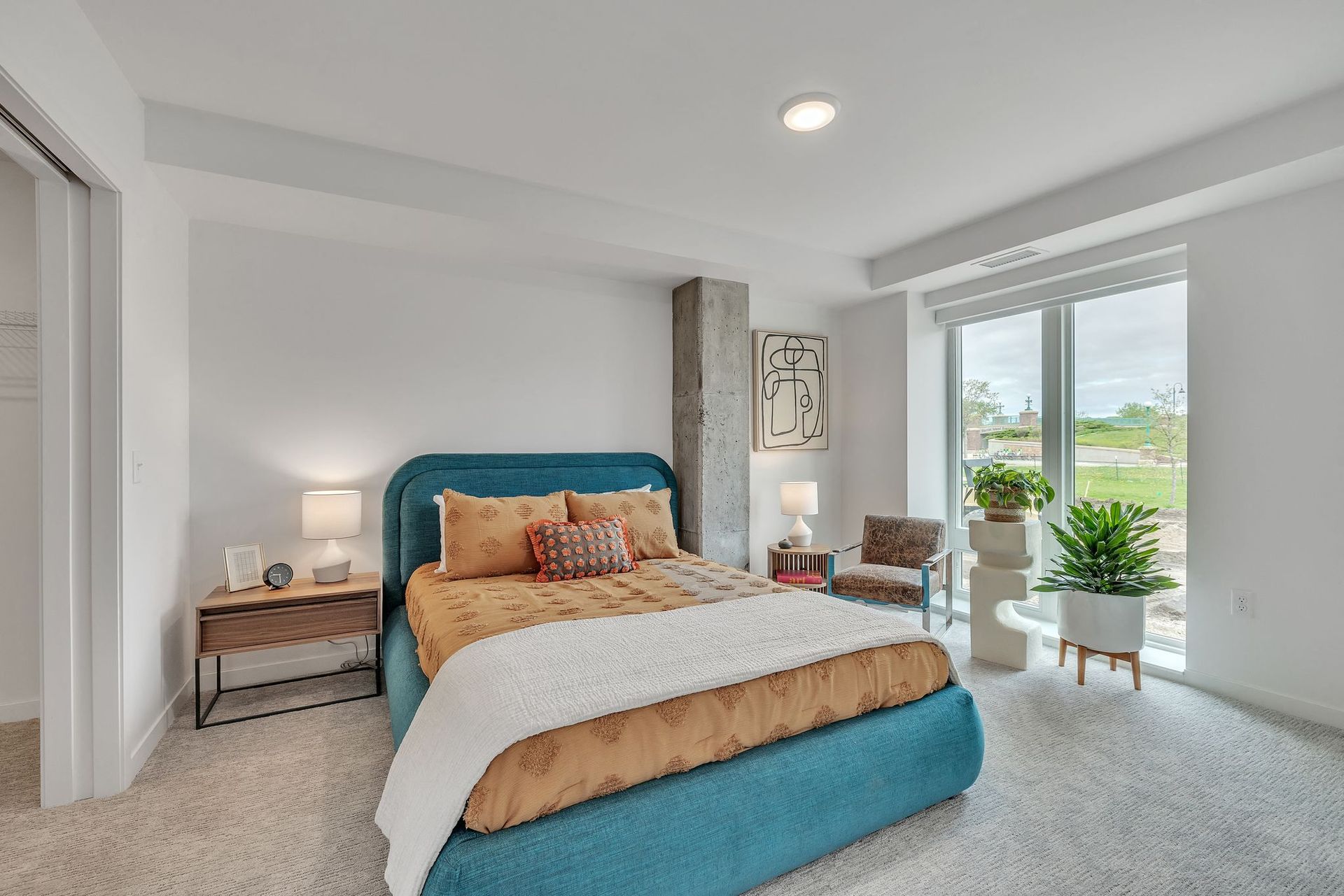Bedroom with turquoise bed, white walls, and a large window overlooking greenery.