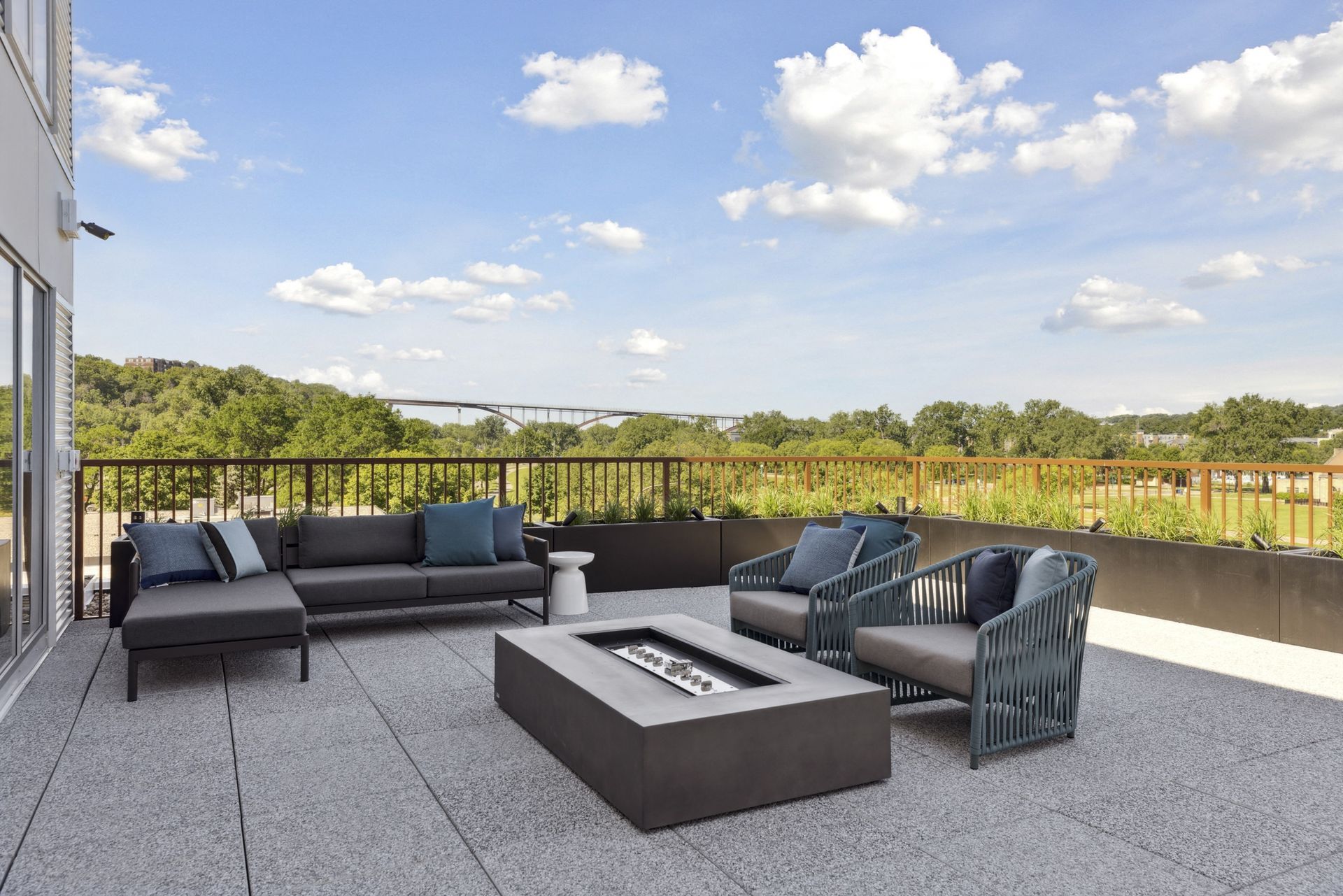 Rooftop patio with dark gray outdoor furniture, fire pit, and a view of trees and sky.