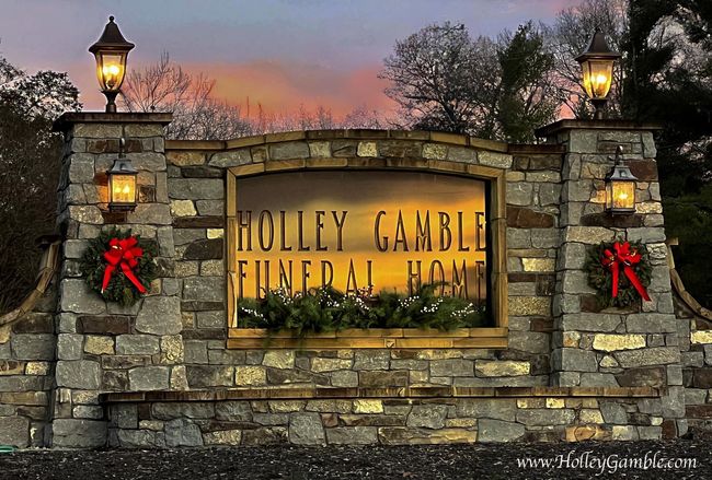Stone entrance sign for Holly Gables at dusk, lit by lanterns and decorated with red bows